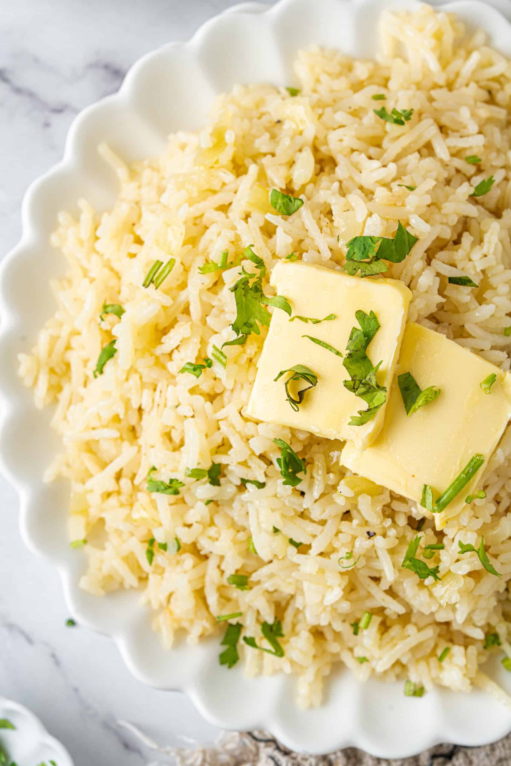 Close-up of butter rice topped with butter slices and fresh parsley.