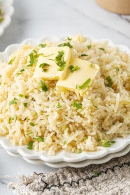 Plate of fluffy butter rice topped with melting butter and fresh parsley.