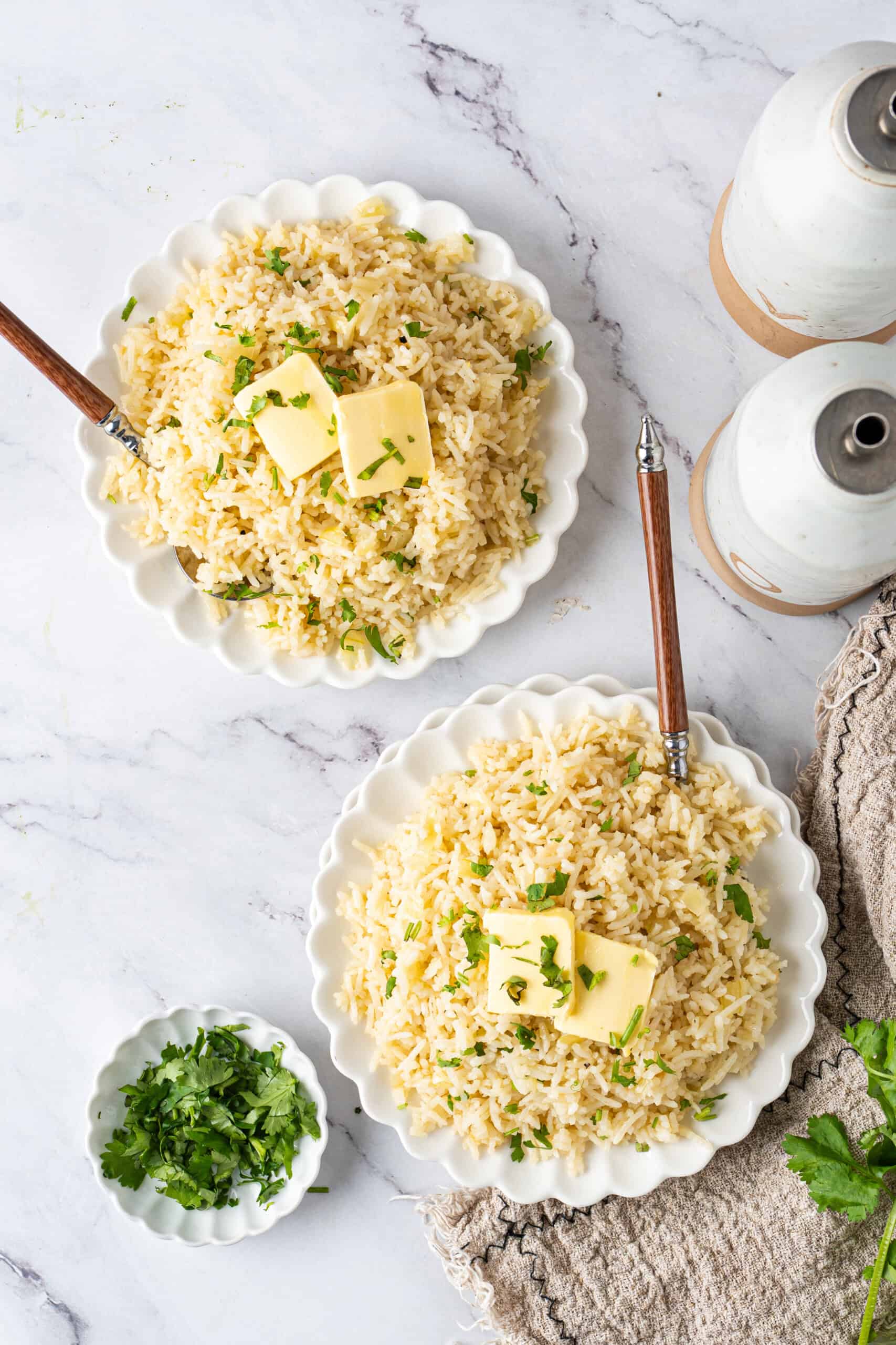 Two bowls of fluffy butter rice topped with butter and parsley, served with fresh chopped parsley on the side.