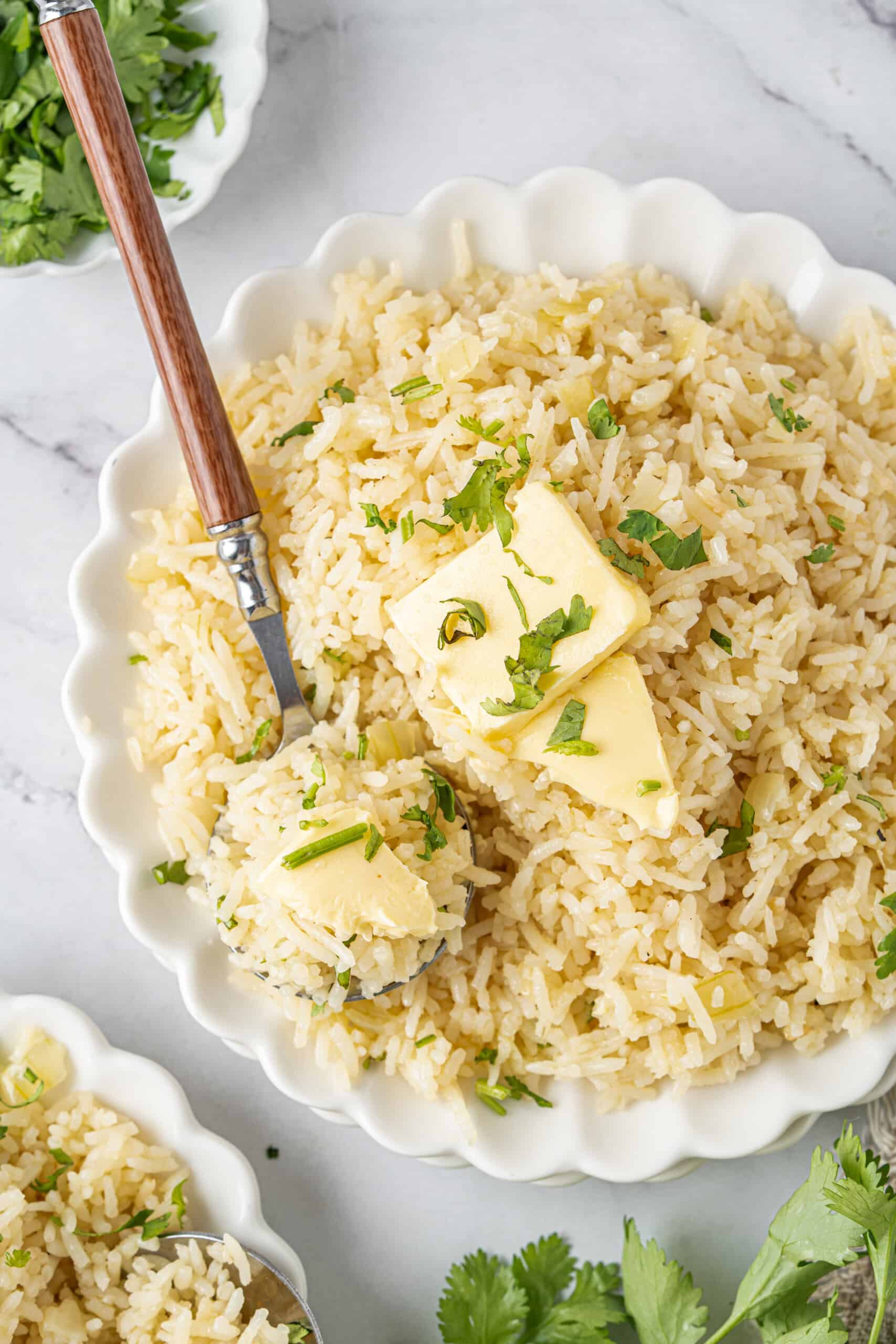 Bowl of fluffy butter rice topped with melting butter and fresh parsley, with a spoonful scooped out for serving.