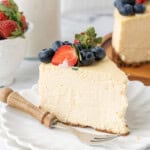 Slice of creamy baked cheesecake topped with fresh strawberries and blueberries on a white dessert plate