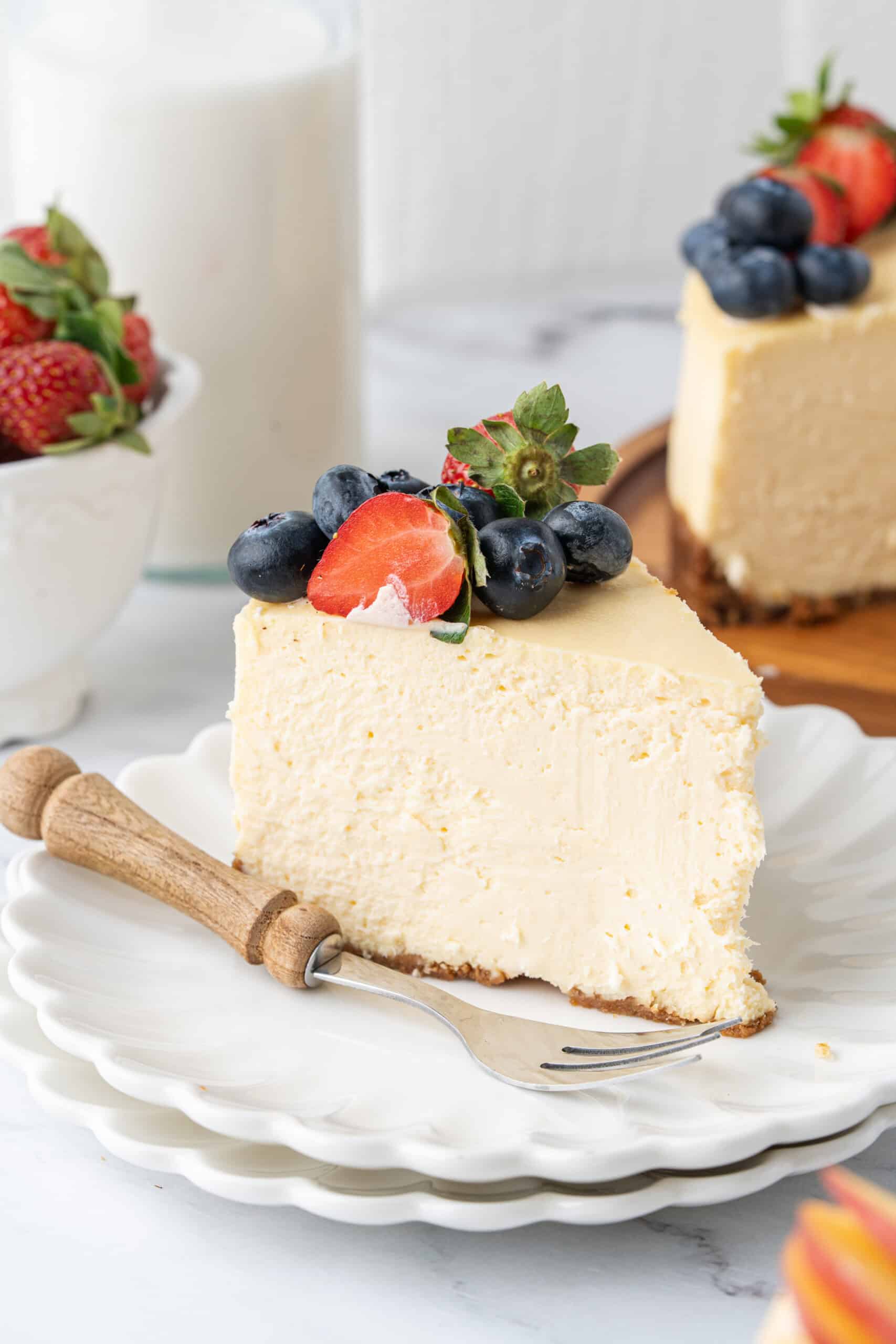 Slice of creamy baked cheesecake topped with fresh strawberries and blueberries on a white dessert plate