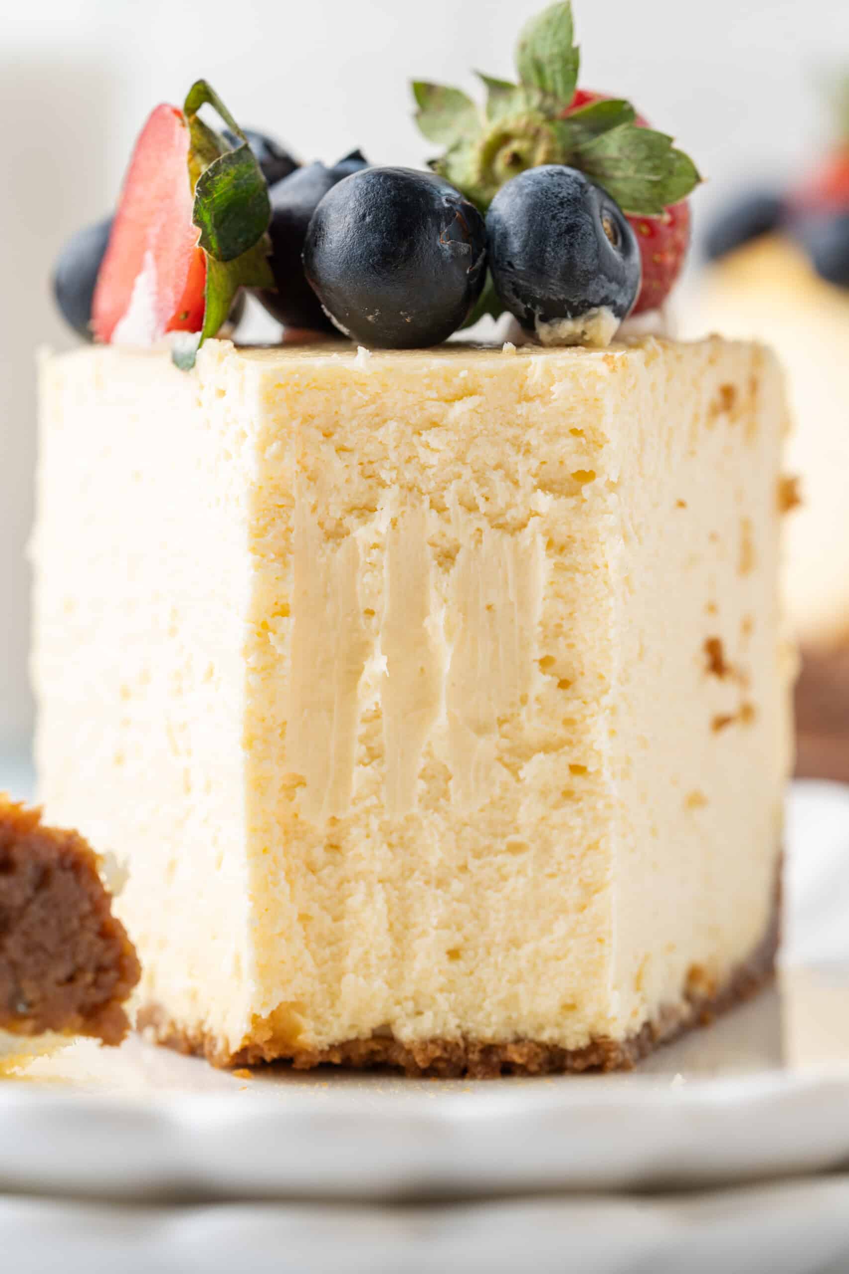 Close-up of a thick slice of creamy baked cheesecake topped with fresh strawberries and blueberries