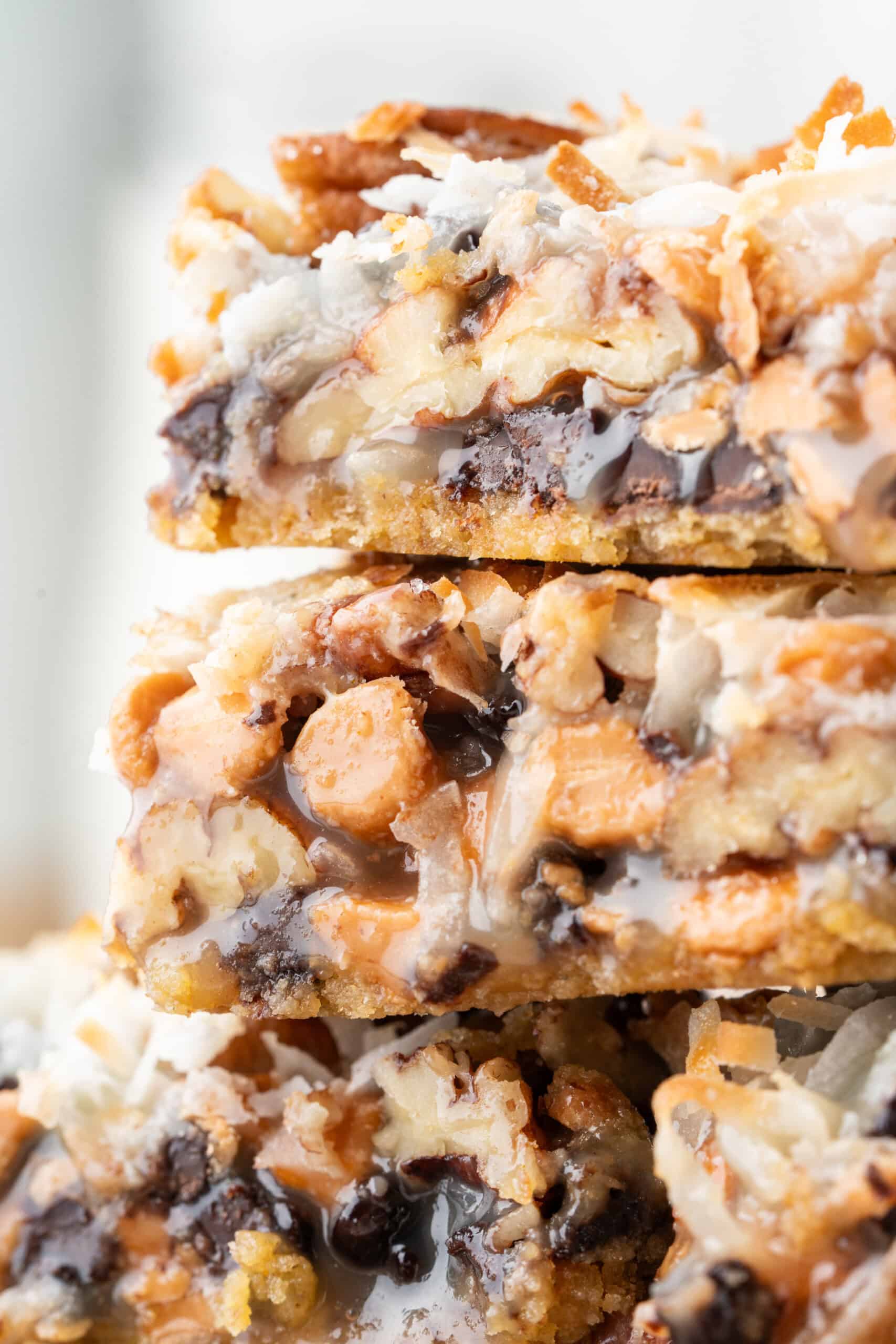 Close-up of stacked 7-Layer Bars showing layers of chocolate chips, butterscotch chips, coconut, pecans, and graham cracker crust.