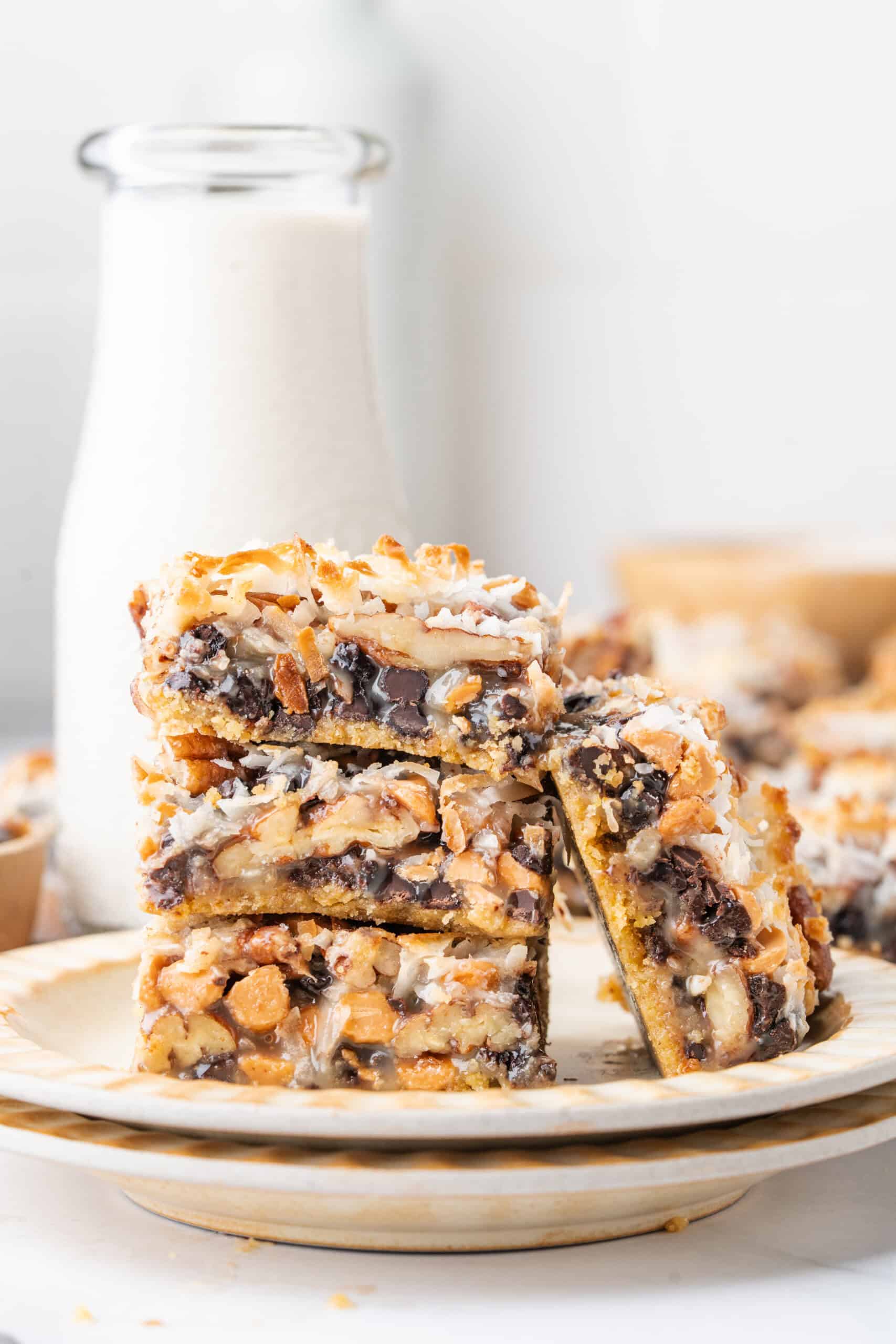 Stack of homemade magic bars on a plate with layers of chocolate chips, butterscotch chips, coconut, pecans, and graham cracker crust.
