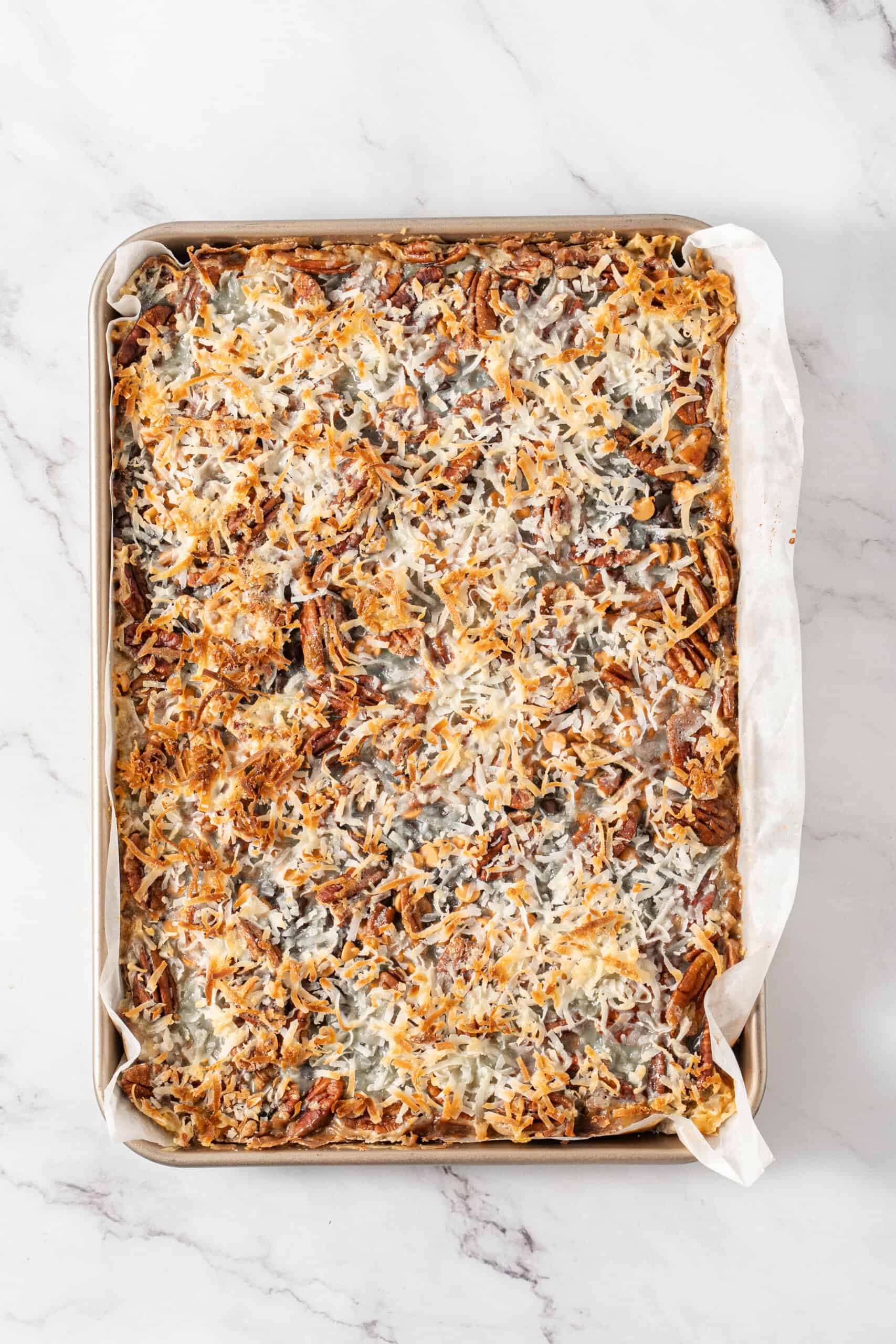 Baked magic bars with toasted coconut and pecans in a parchment-lined baking pan.