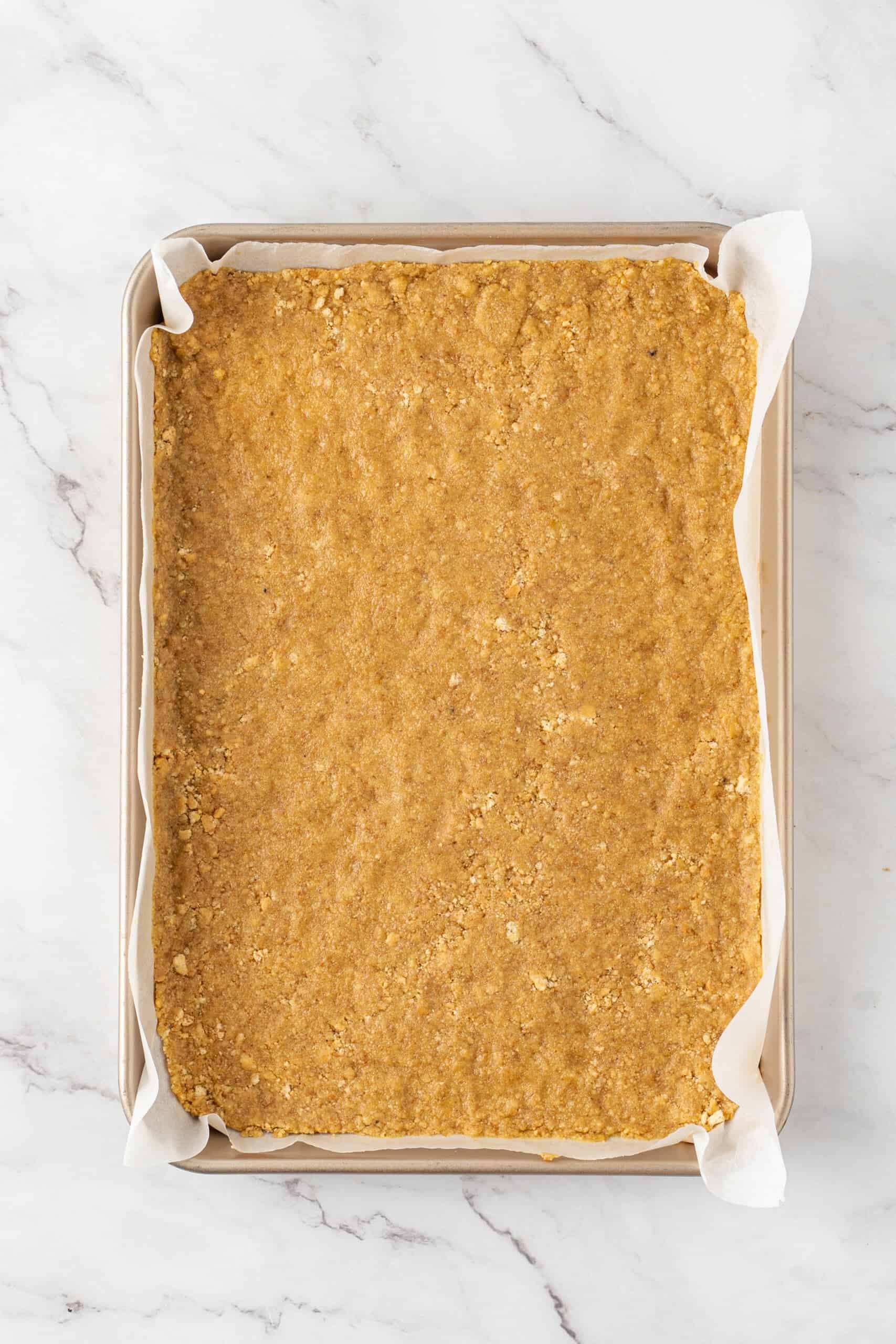 Pressed graham cracker crust in a parchment-lined baking pan