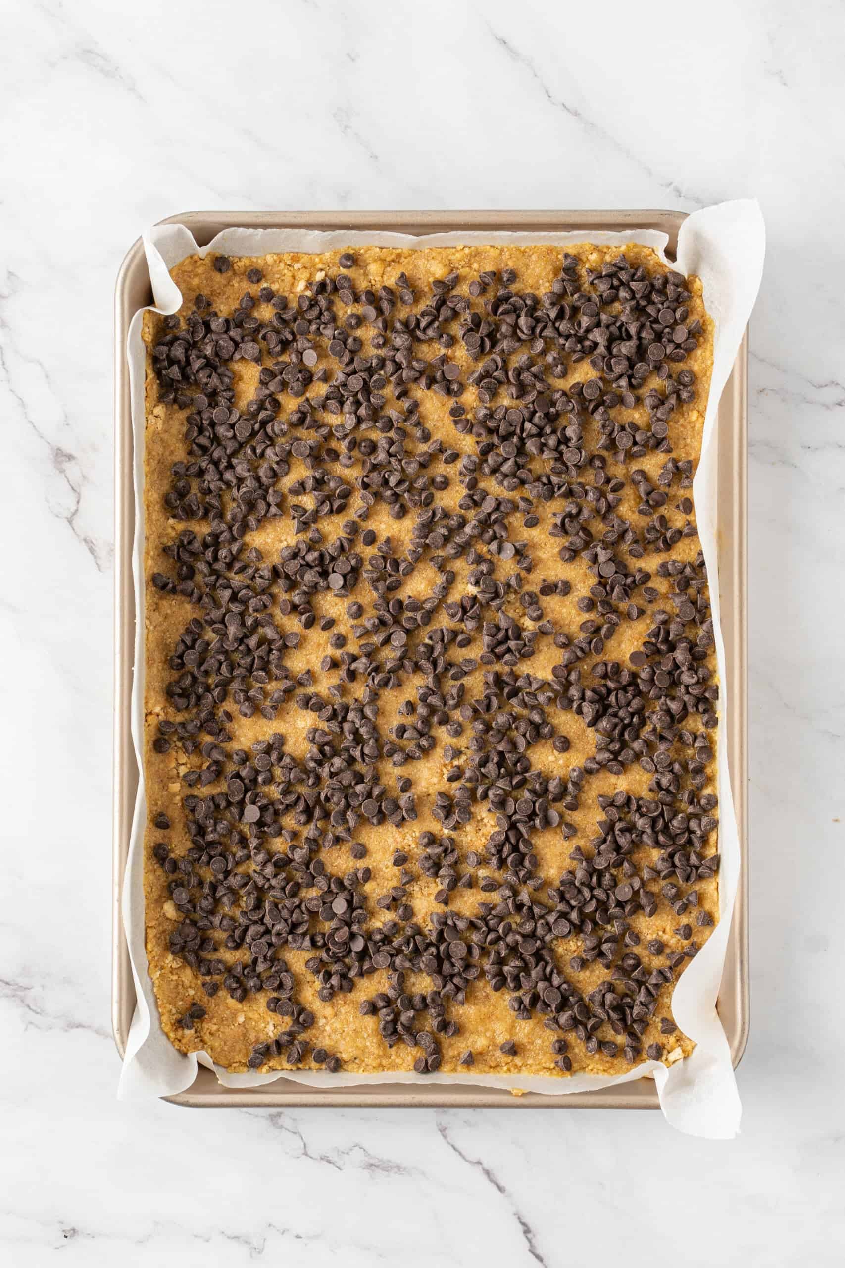 Chocolate chips sprinkled over a graham cracker crust in a parchment-lined pan