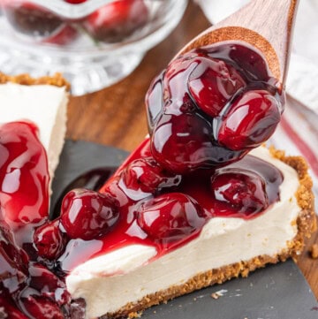 Spoonful of cherry pie filling being added to a slice of no-bake cheesecake with a graham cracker crust.