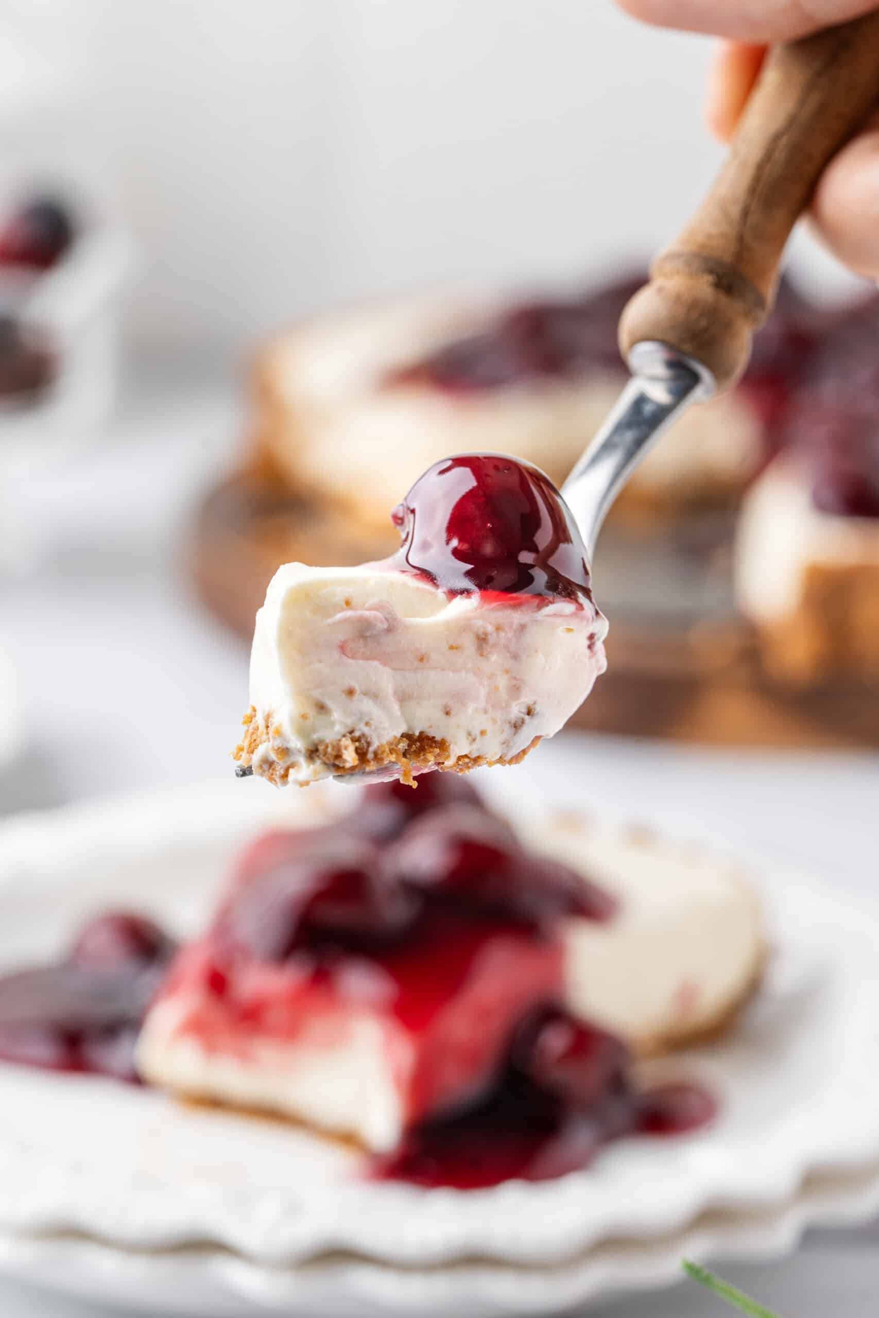 Bite of no-bake cheesecake with graham cracker crust and cherry pie filling held on a dessert fork.