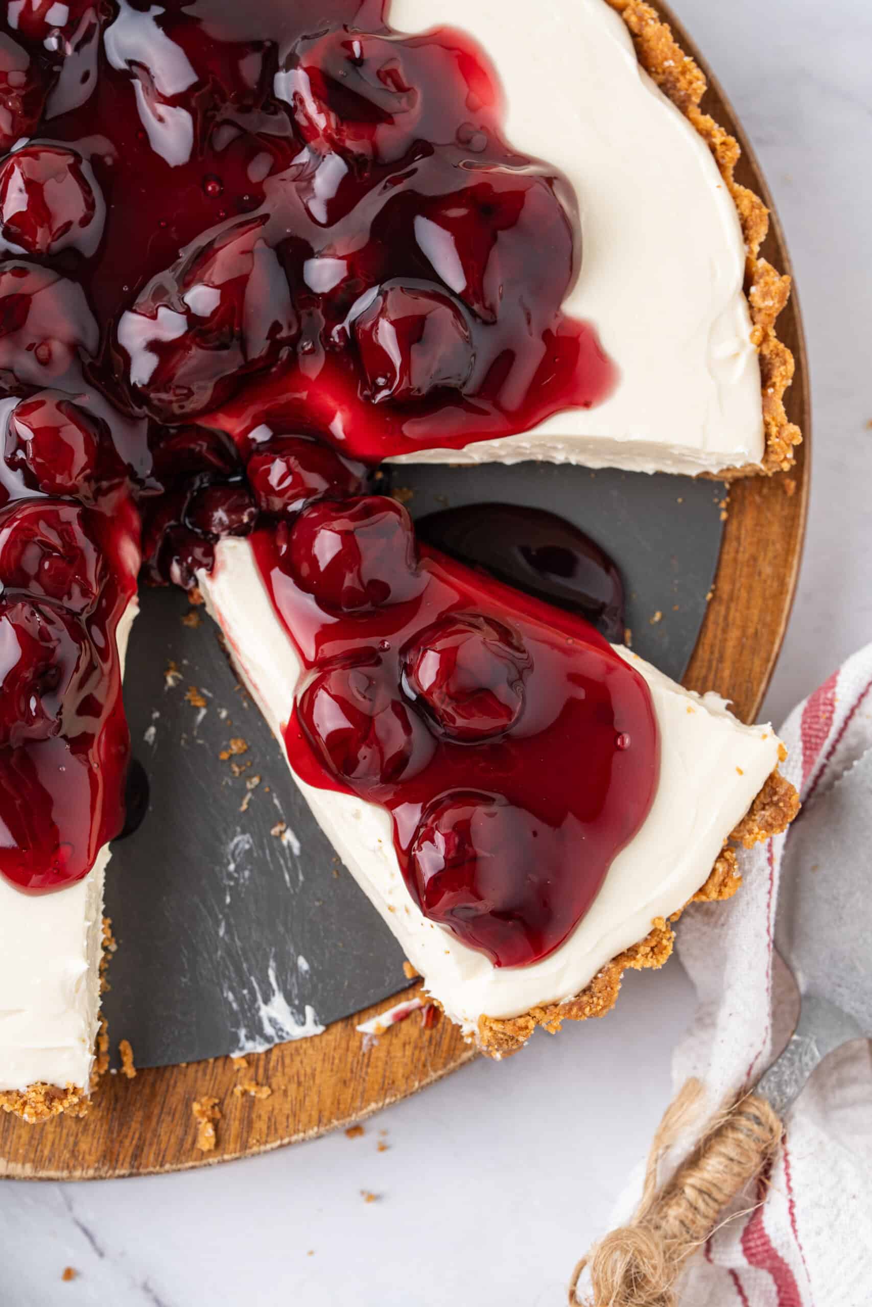 Close-up of a slice of no-bake cheesecake topped with cherry pie filling being lifted from the cheesecake with a cake server.