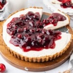 No-bake cheesecake topped with cherry pie filling, with one slice removed and served alongside the remaining cheesecake.