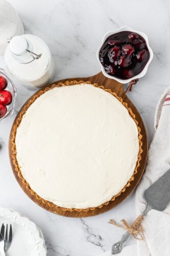 Chilled no-bake cheesecake in a graham cracker crust with a bowl of cherry topping on the side