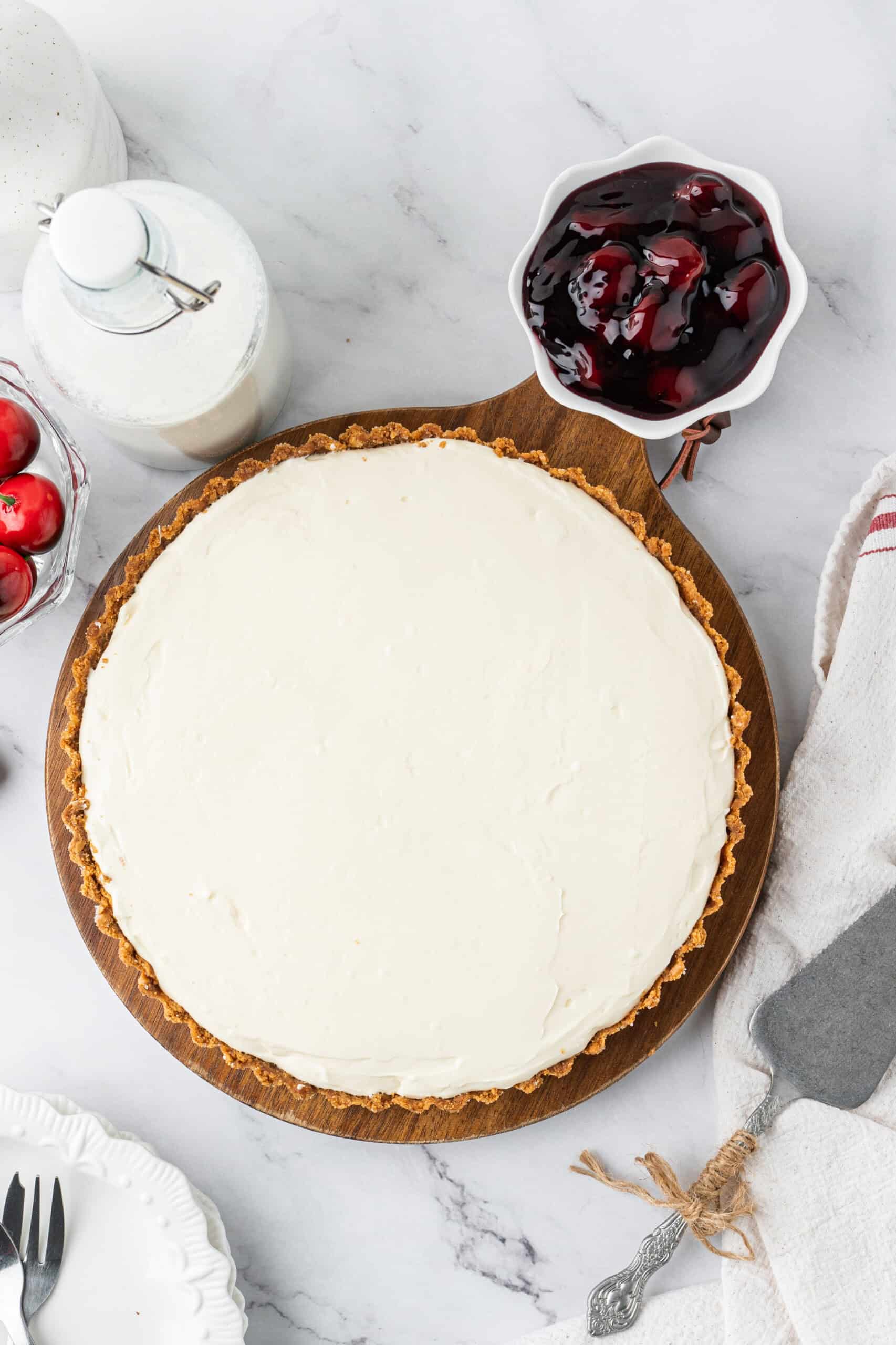 Chilled no-bake cheesecake in a graham cracker crust with a bowl of cherry topping on the side