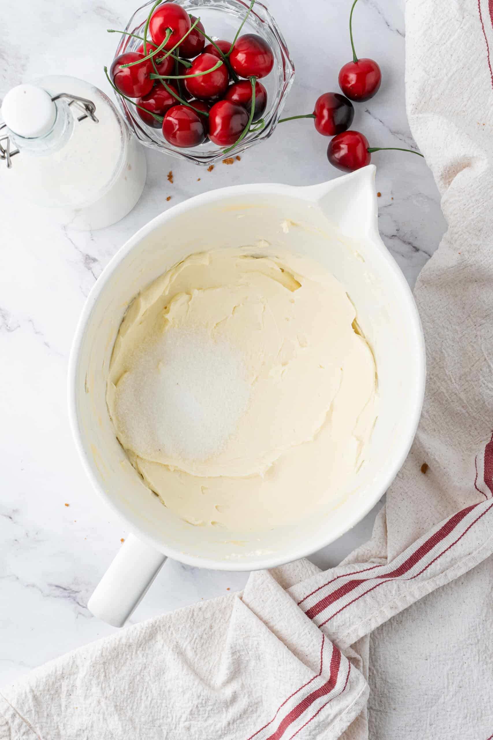 Cream cheese and granulated sugar in a mixing bowl before being beaten together for no-bake cheesecake filling.