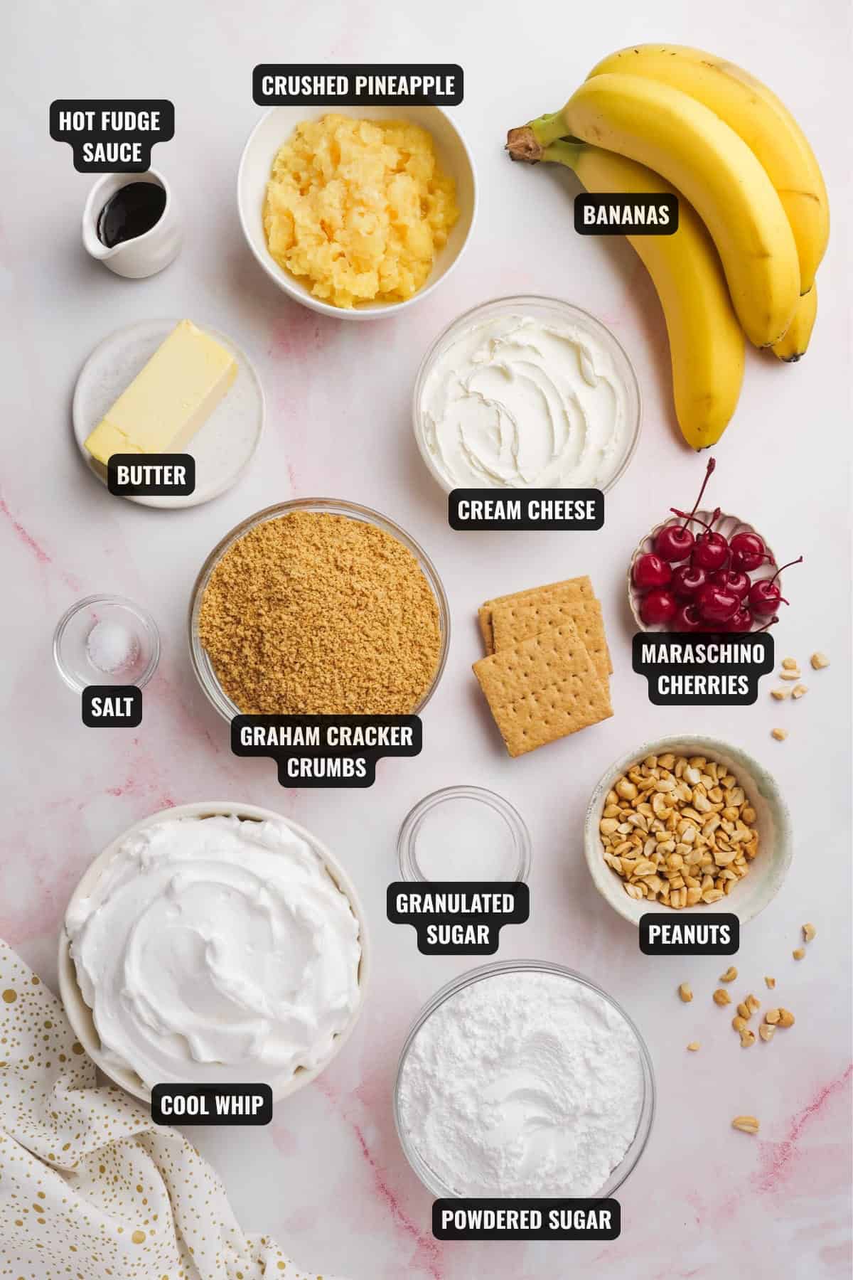 ingredients for banana split cake recipe including bananas, pineapple, cream cheese, graham cracker crumbs, peanuts, cool whip, cherries, butter, hot fudge sauce, and sugar