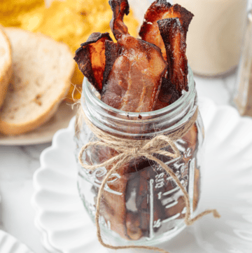 Crispy bacon strips standing upright in a glass jar.