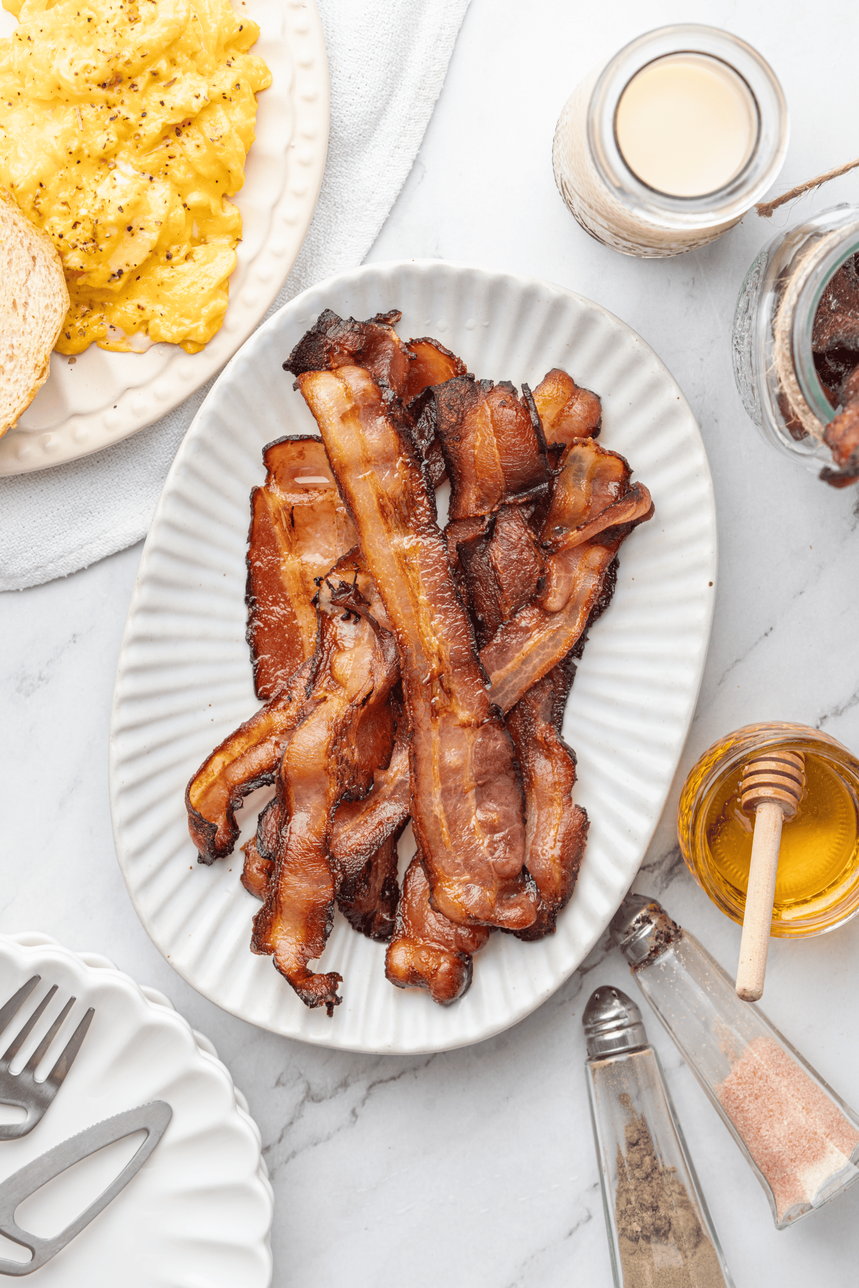 Crispy bacon strips on a white platter with scrambled eggs and toast.