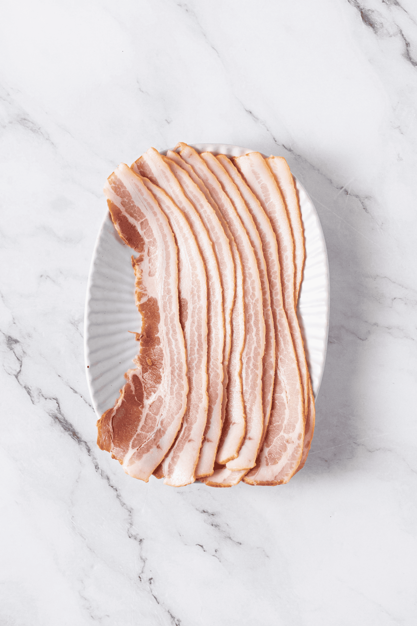 Raw bacon strips arranged on a white plate.