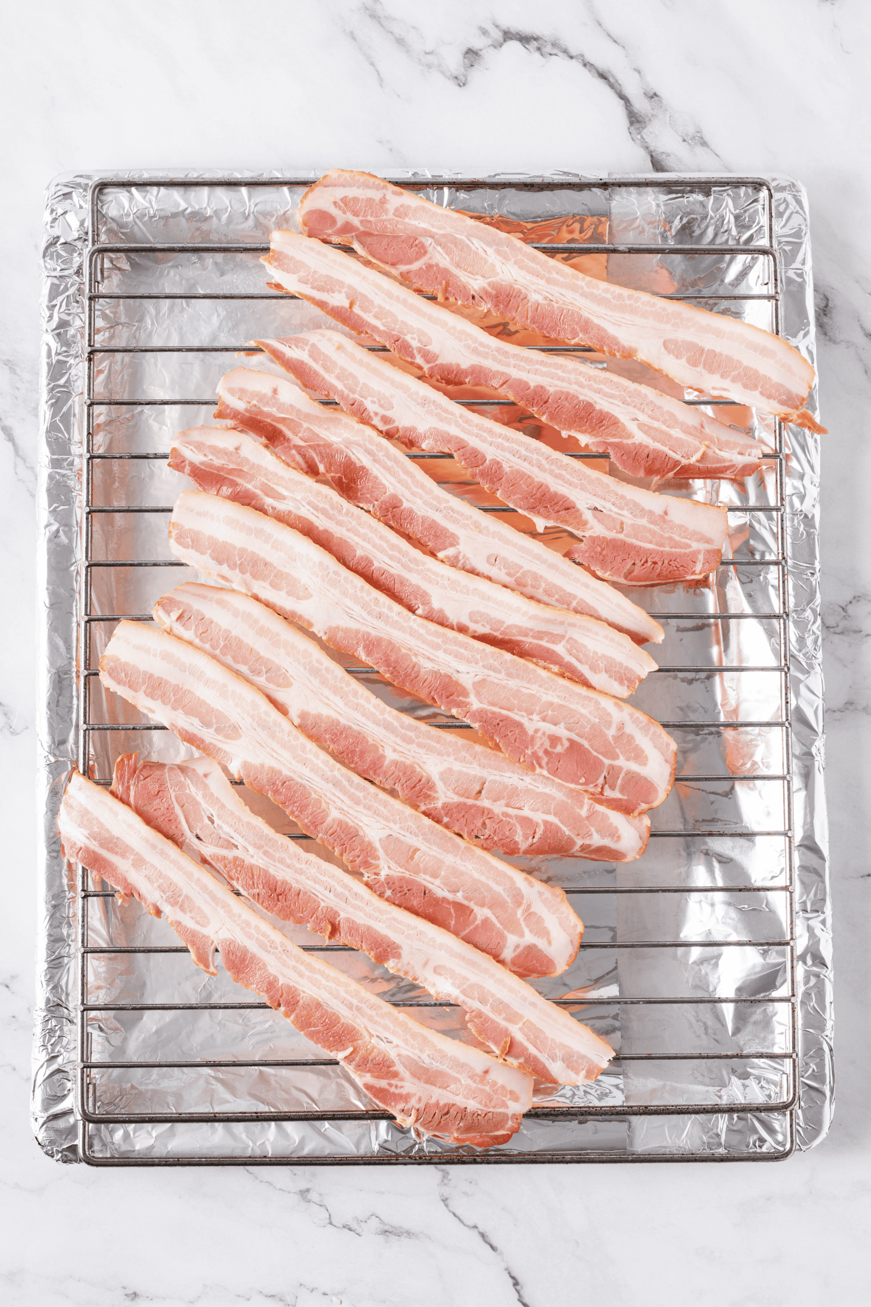 Raw bacon strips arranged on a wire rack over a foil-lined baking sheet.
