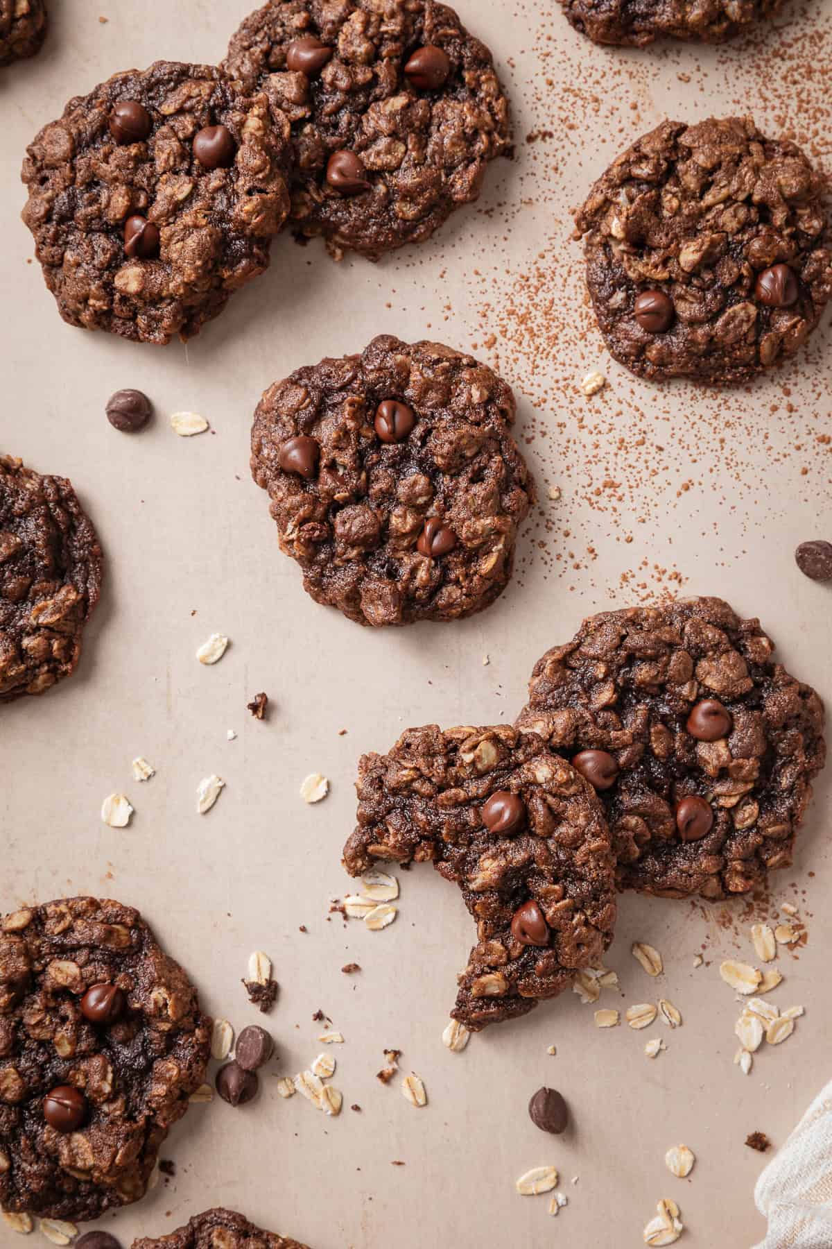 Chocolate oatmeal cookies with chocolate chips, scattered oats, and a broken cookie showing the soft, chewy center.