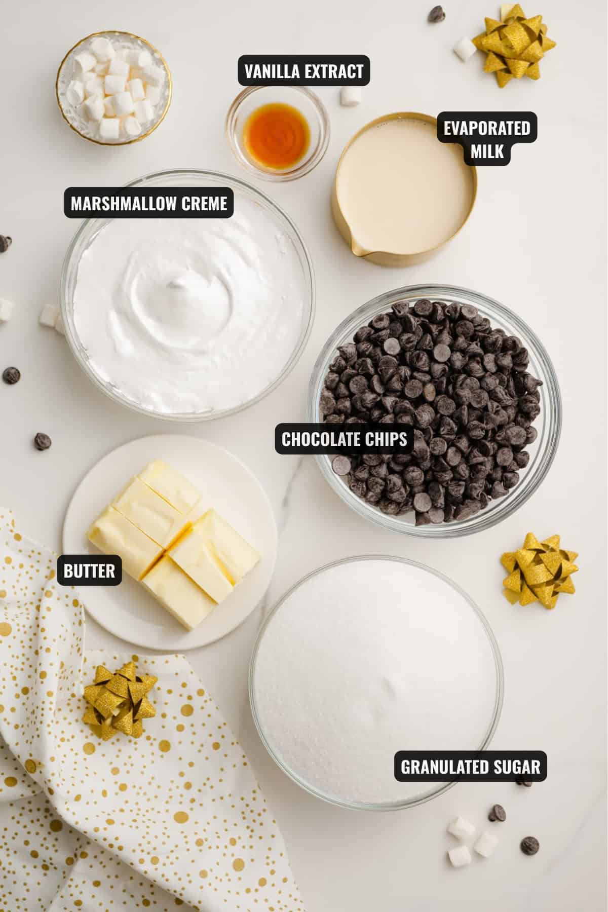 ingredients for fudge recipe including marshmallow creme, chocolate chips, vanilla extract, evaporated milk, butter, and granulated sugar.