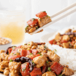 Kung Pao chicken served over white rice with red bell peppers, peanuts, dried chilies, and green onions.
