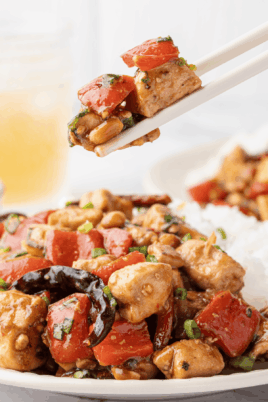 Kung Pao chicken served over white rice with red bell peppers, peanuts, dried chilies, and green onions.