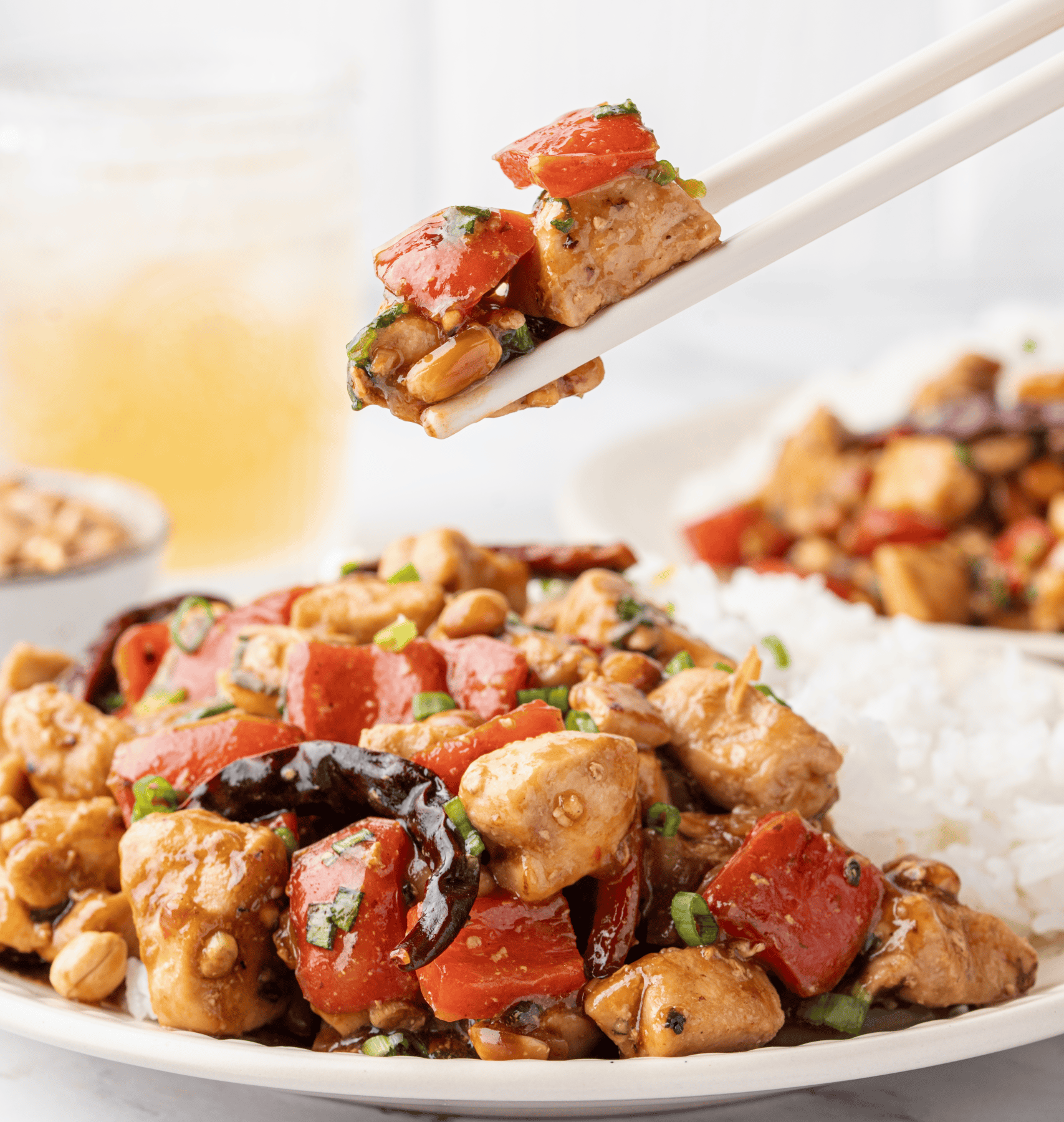Kung Pao chicken served over white rice with red bell peppers, peanuts, dried chilies, and green onions.