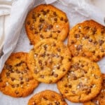 Golden chocolate chip cookies sprinkled with flaky sea salt on parchment paper.