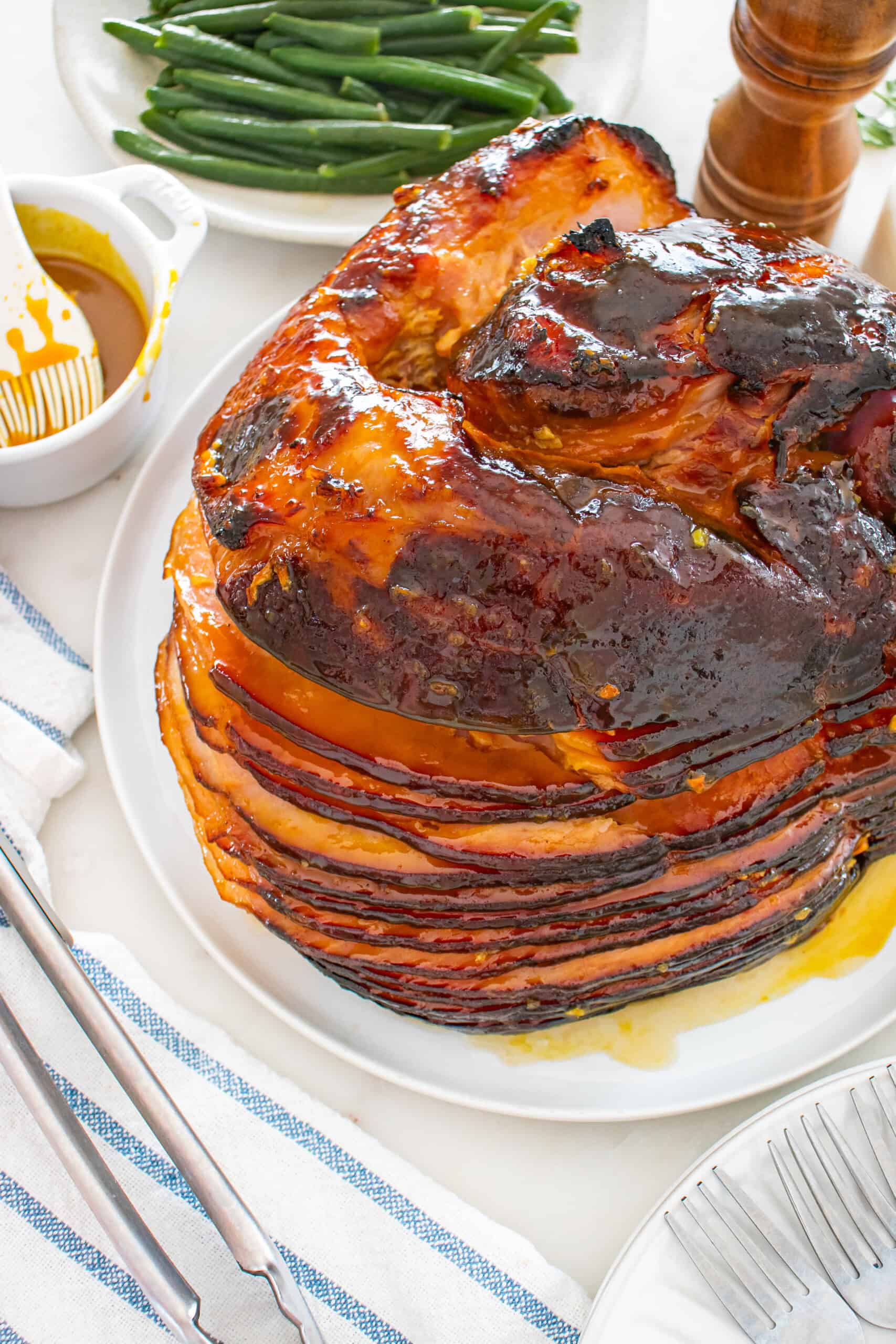 Close-up of glazed baked ham on a serving platter with green beans and extra glaze.