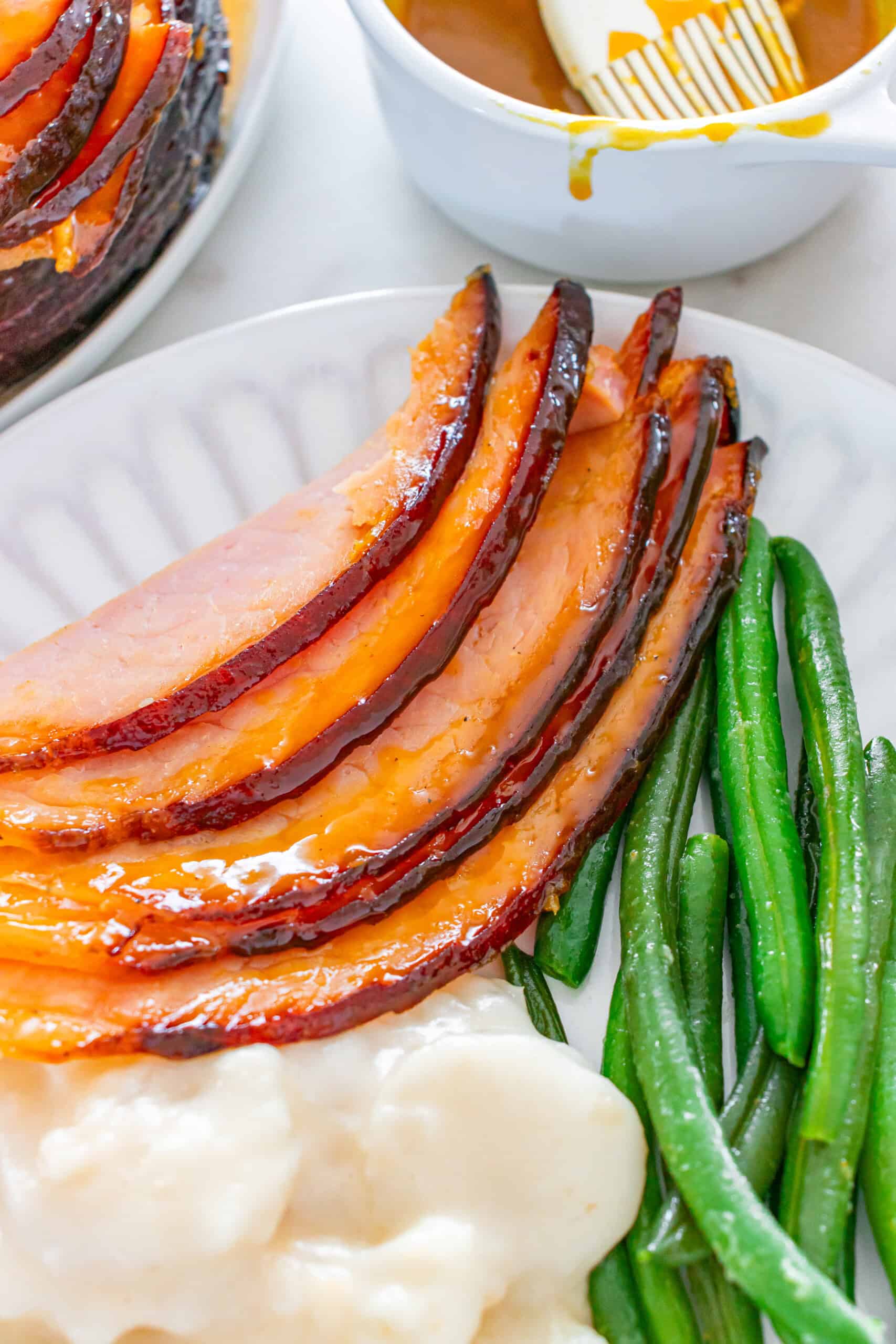 Slices of glazed ham served with green beans and mashed potatoes.
