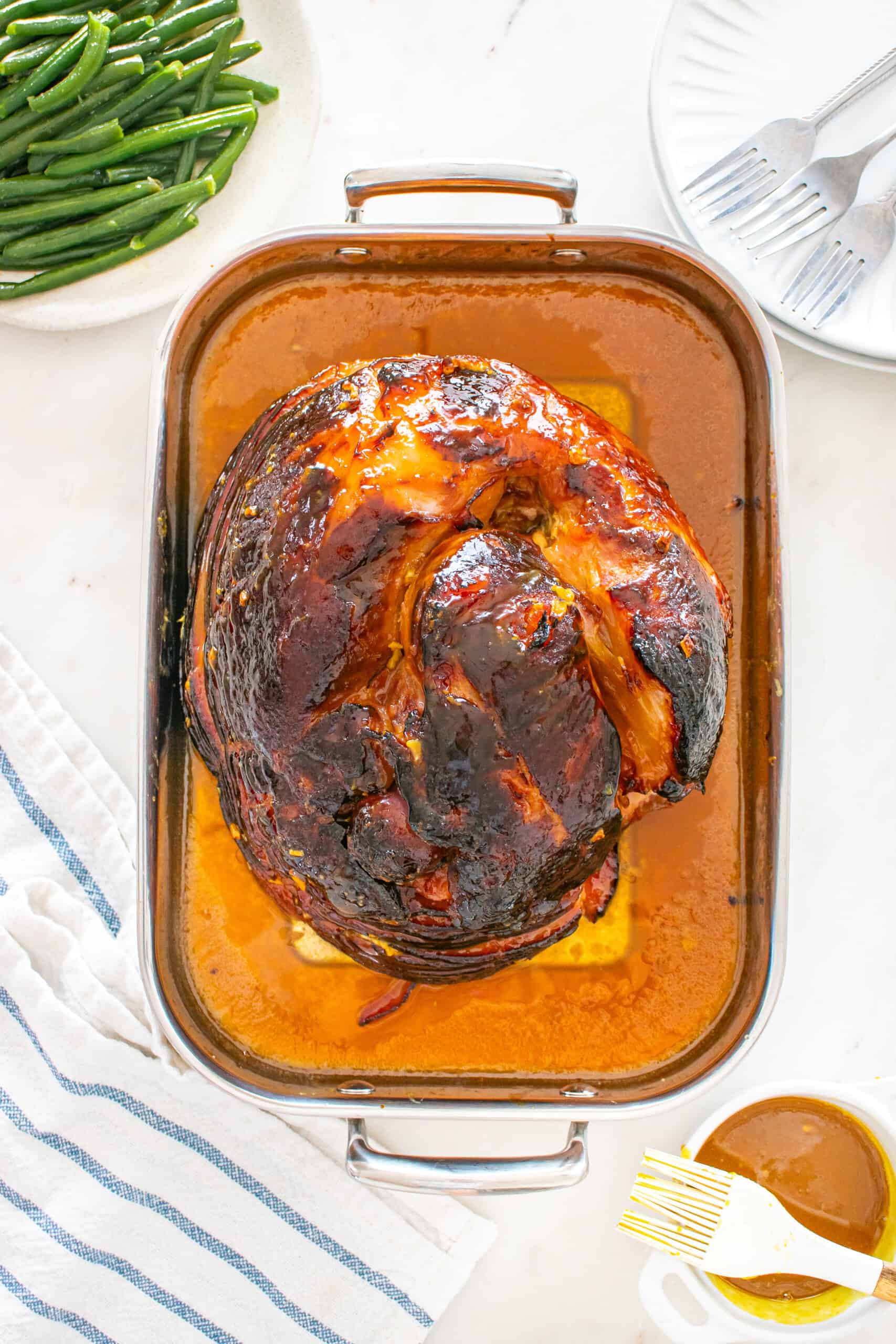 Glazed spiral ham in a roasting pan served with green beans.