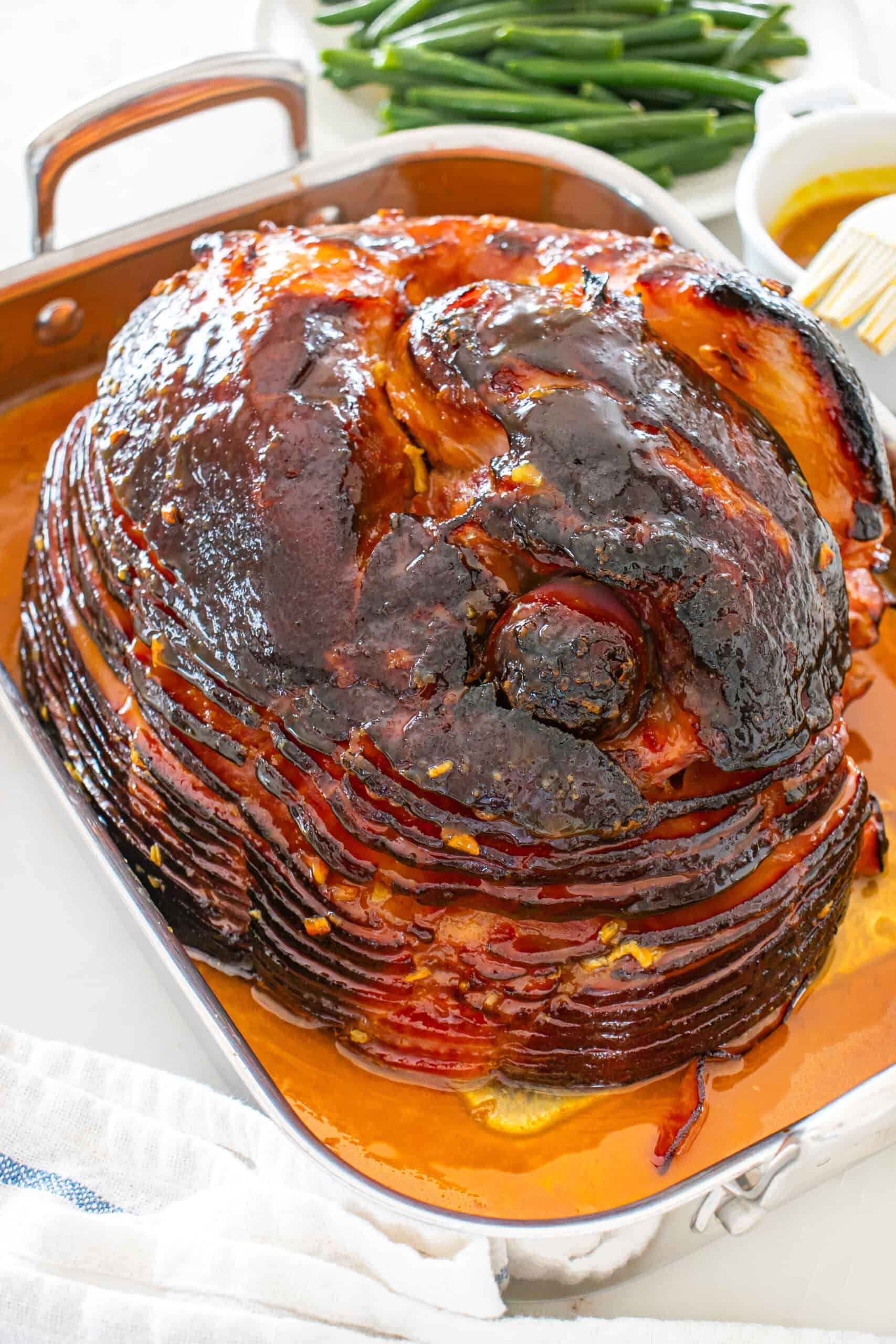 Glazed spiral ham in a roasting pan with green beans and extra glaze.