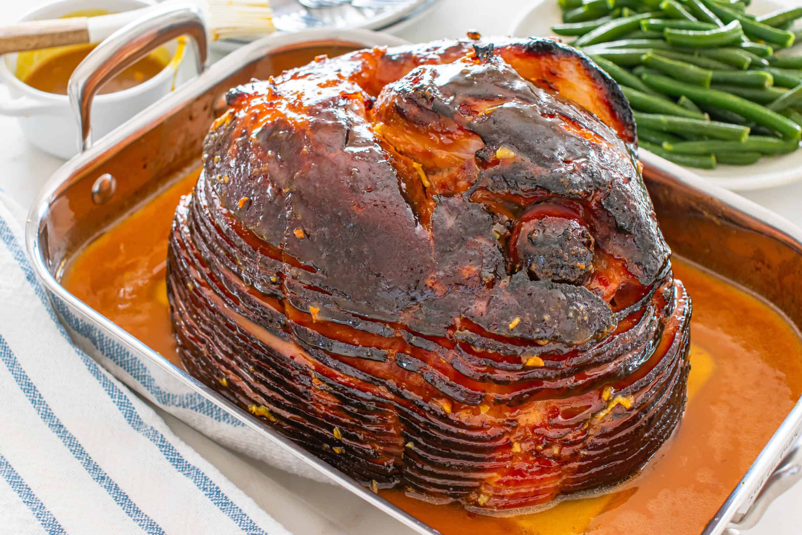 Glazed baked ham in a roasting pan with green beans and extra glaze.