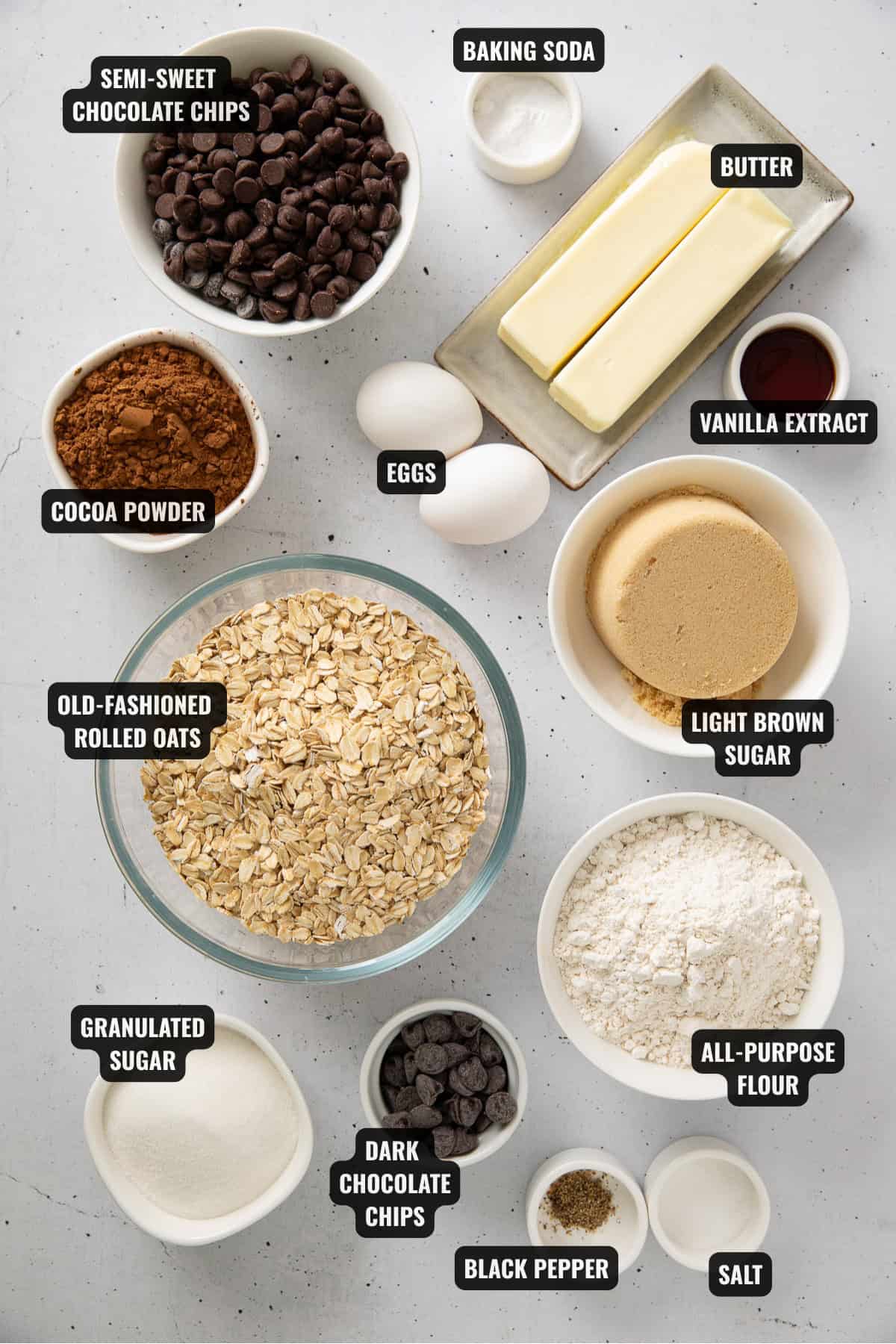 ingredients for chocolate oatmeal cookies recipe including oats, flour, sugar, chocolate chips, eggs, butter, baking soda, cocoa powder, vanilla extract, black pepper and salt.