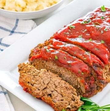 Sliced meatloaf with glaze and parsley, served with mashed potatoes and green beans.