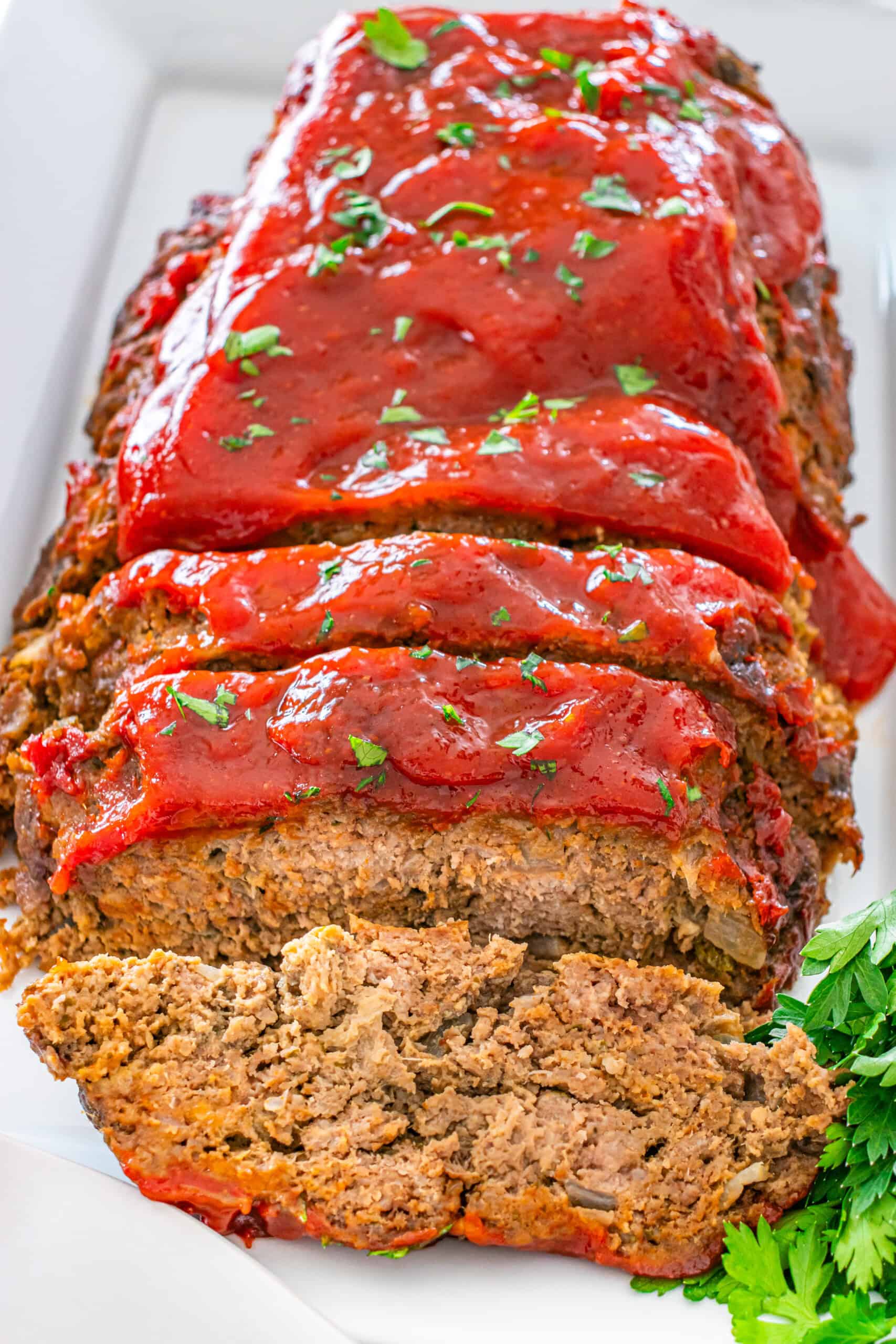 Sliced meatloaf topped with glaze and fresh parsley.