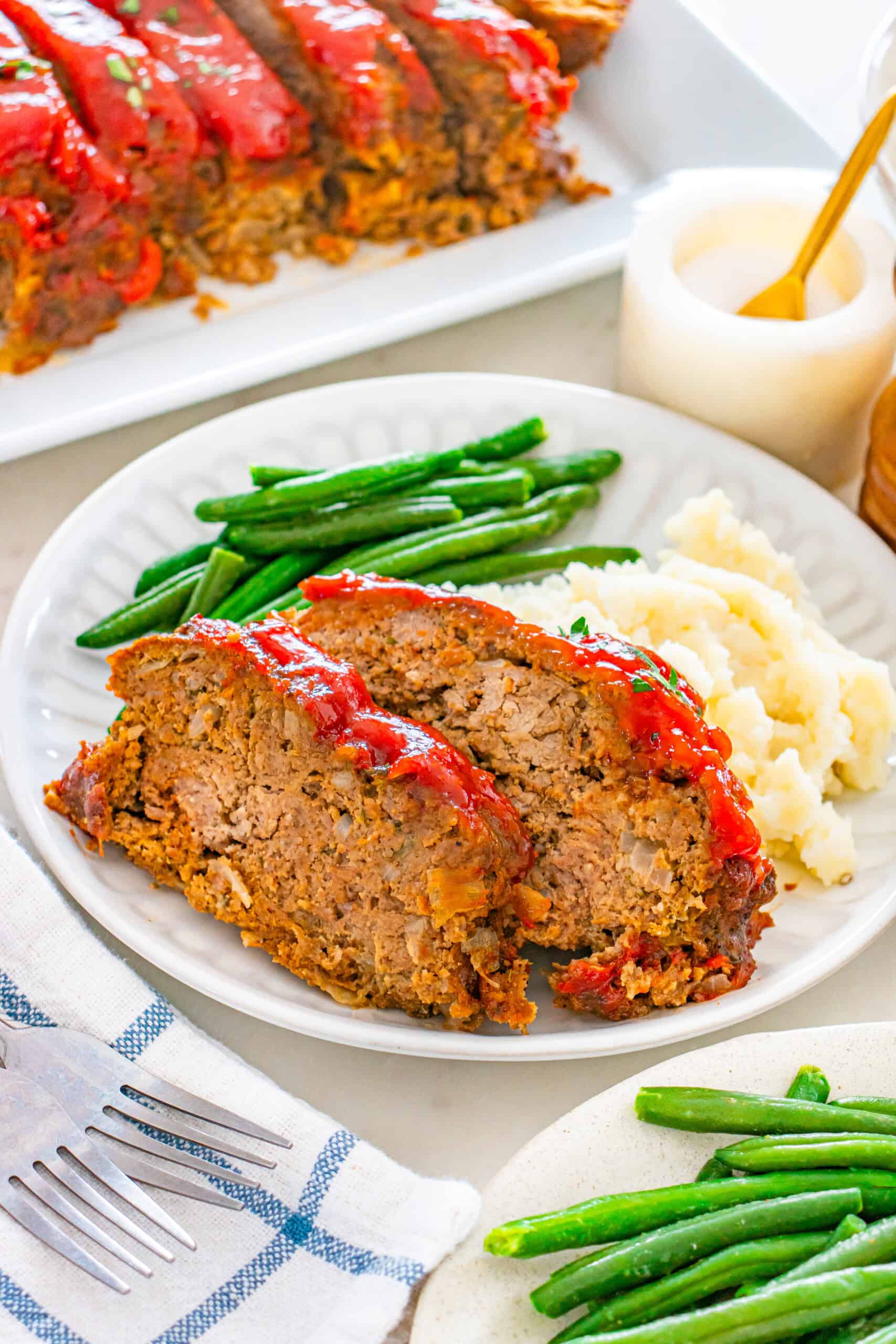 Sliced moist meatloaf with glaze served with mashed potatoes and green beans.