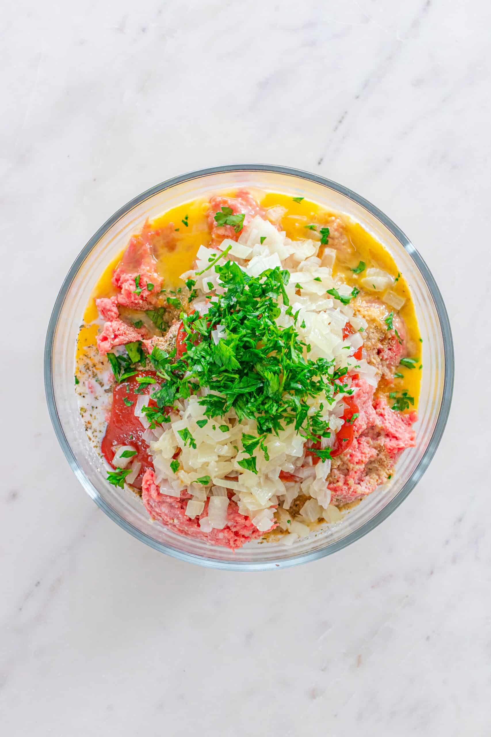 Meatloaf mixture with sautéed onions, ground beef, parsley, eggs, and seasonings in a mixing bowl.