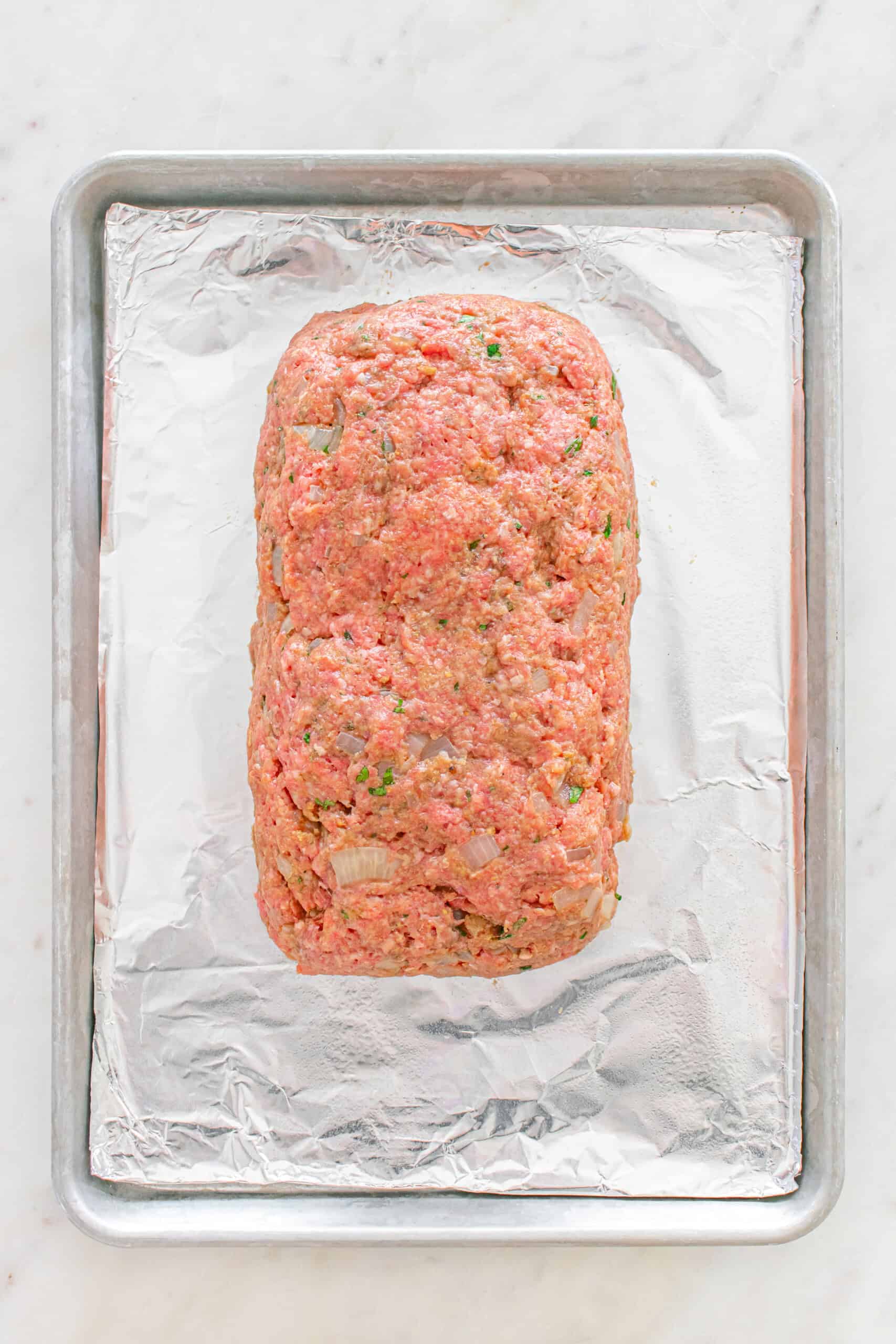 Uncooked meatloaf shaped into a loaf on a foil-lined baking sheet.