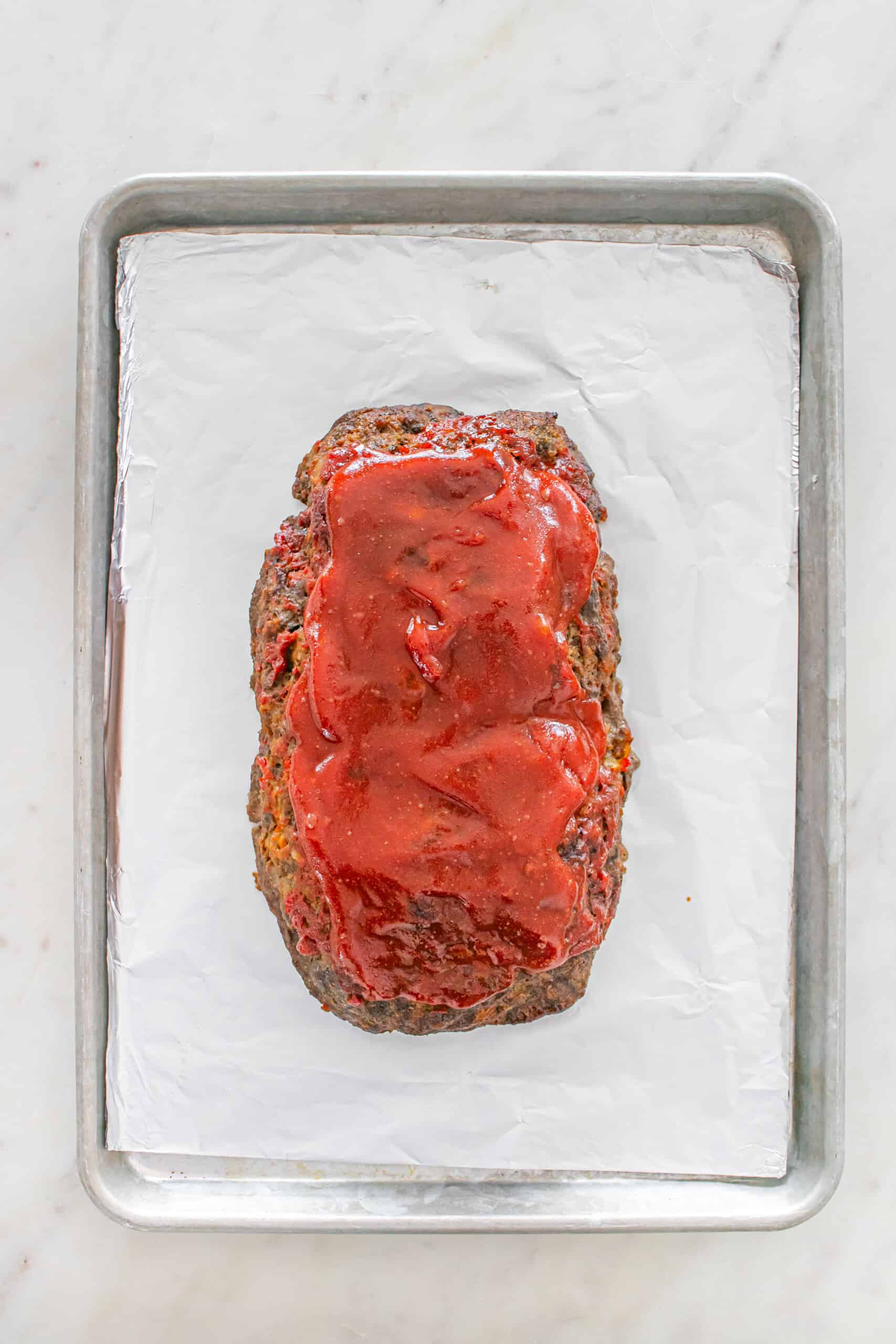 Baked meatloaf topped with glaze on a foil-lined baking sheet.
