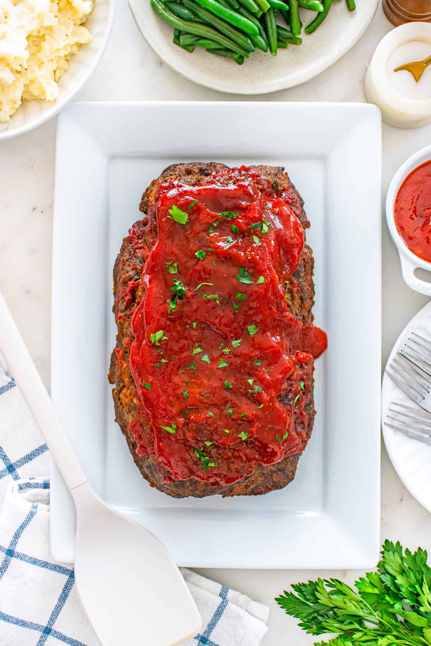Baked moist meatloaf topped with glaze and fresh parsley on a white serving platter.