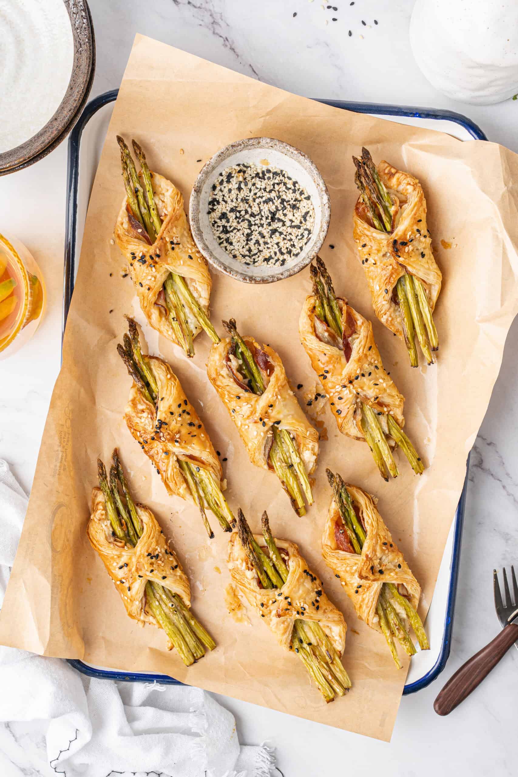 Baked asparagus puff pastry bundles with pancetta and sesame seeds arranged on a serving tray.