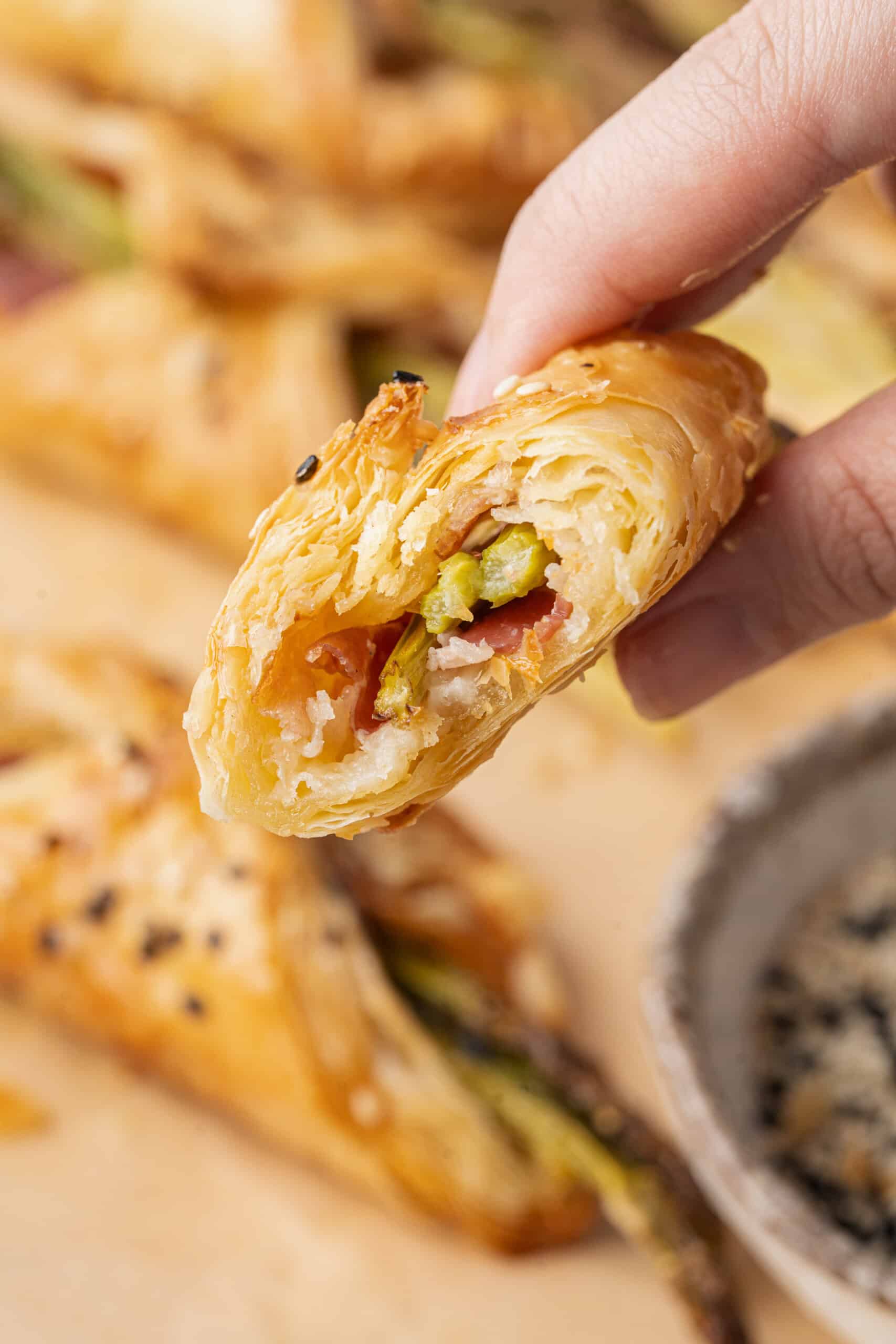 Close-up of a flaky asparagus and pancetta puff pastry bundle held in hand.