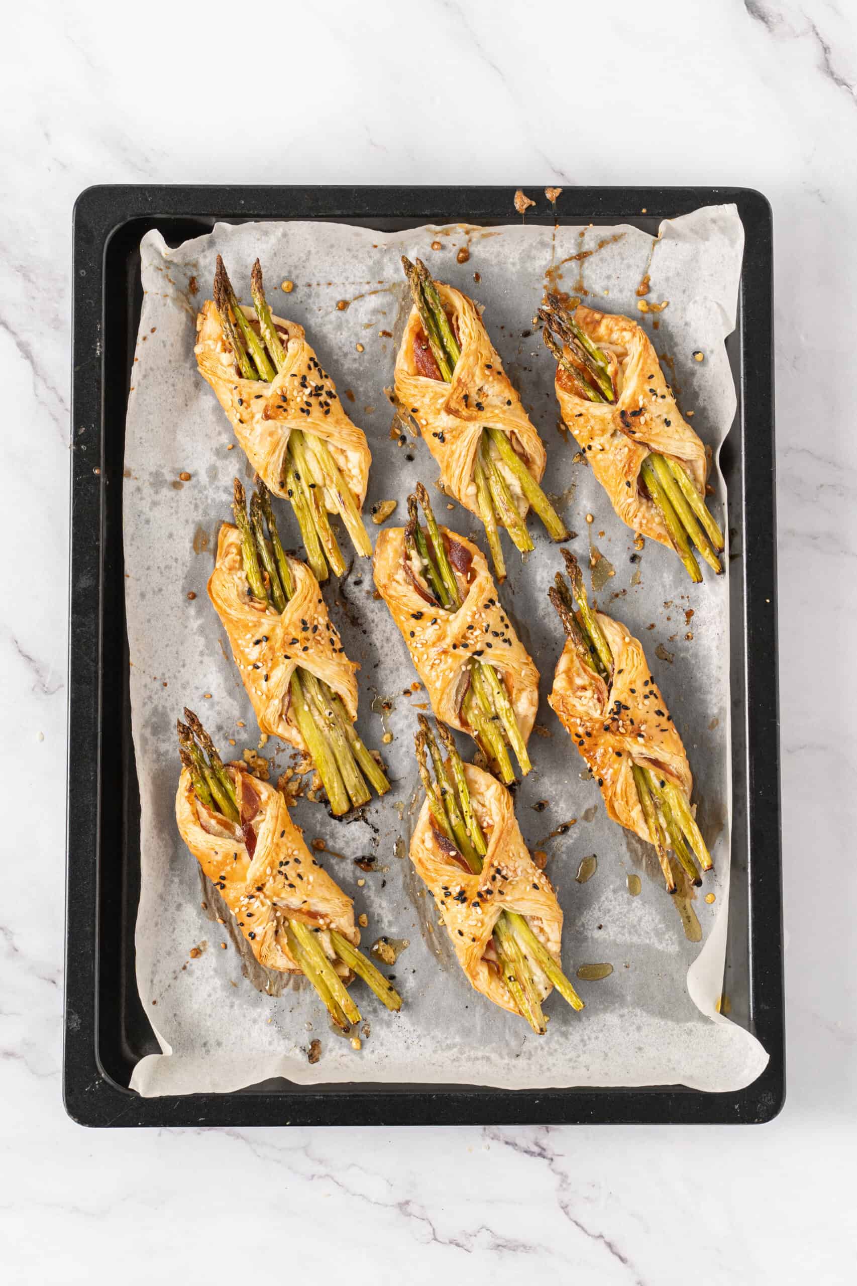 Baked asparagus puff pastry with pancetta and sesame seeds on a baking sheet.