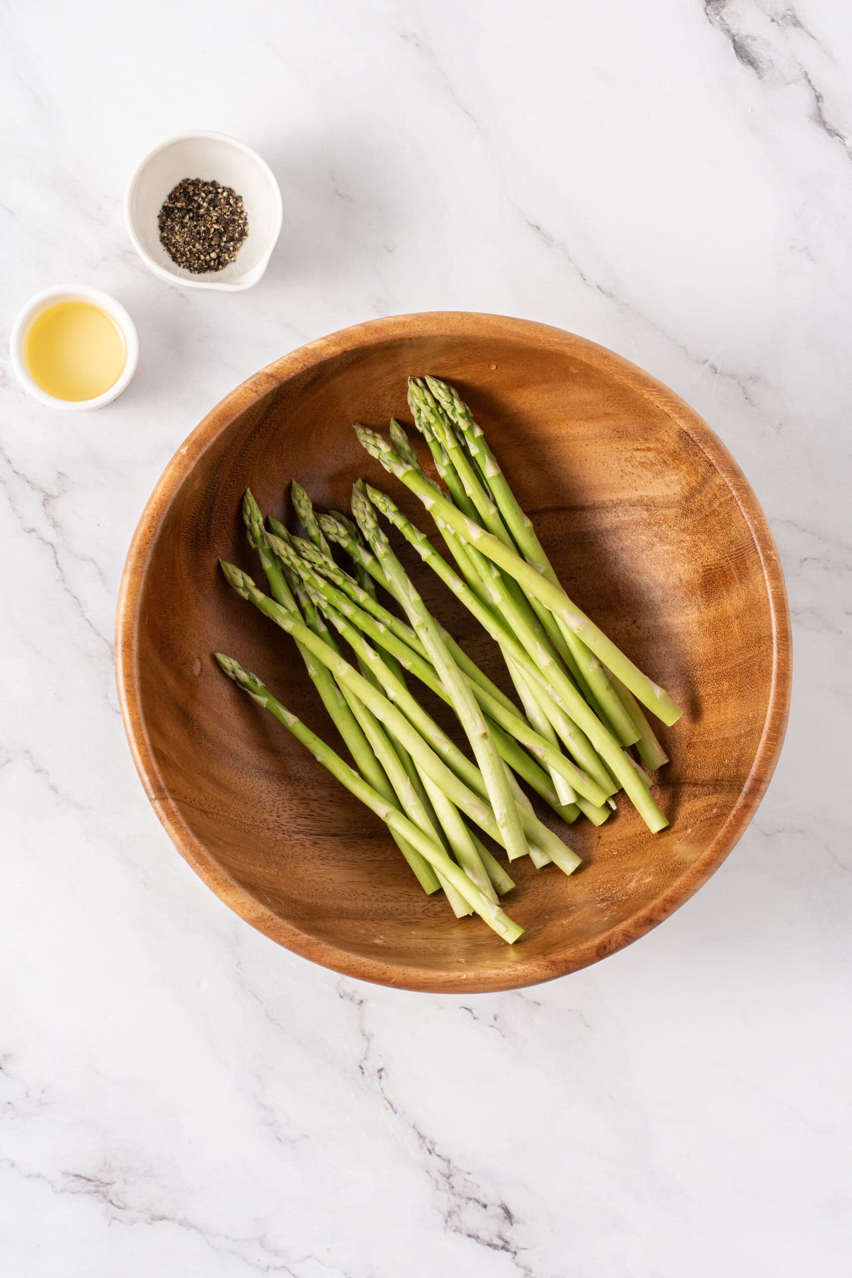 Fresh asparagus spears in a wooden bowl with olive oil and black pepper.