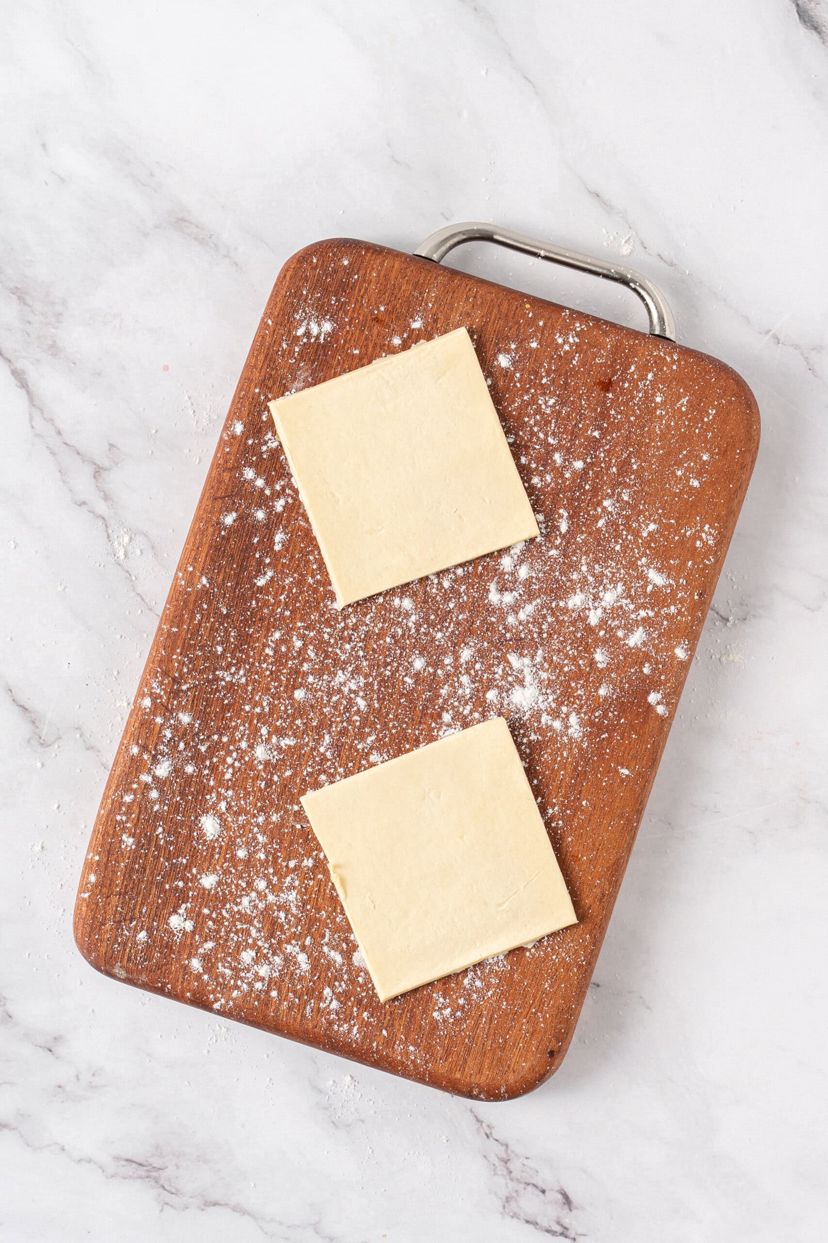 Two puff pastry squares on a lightly floured wooden cutting board.