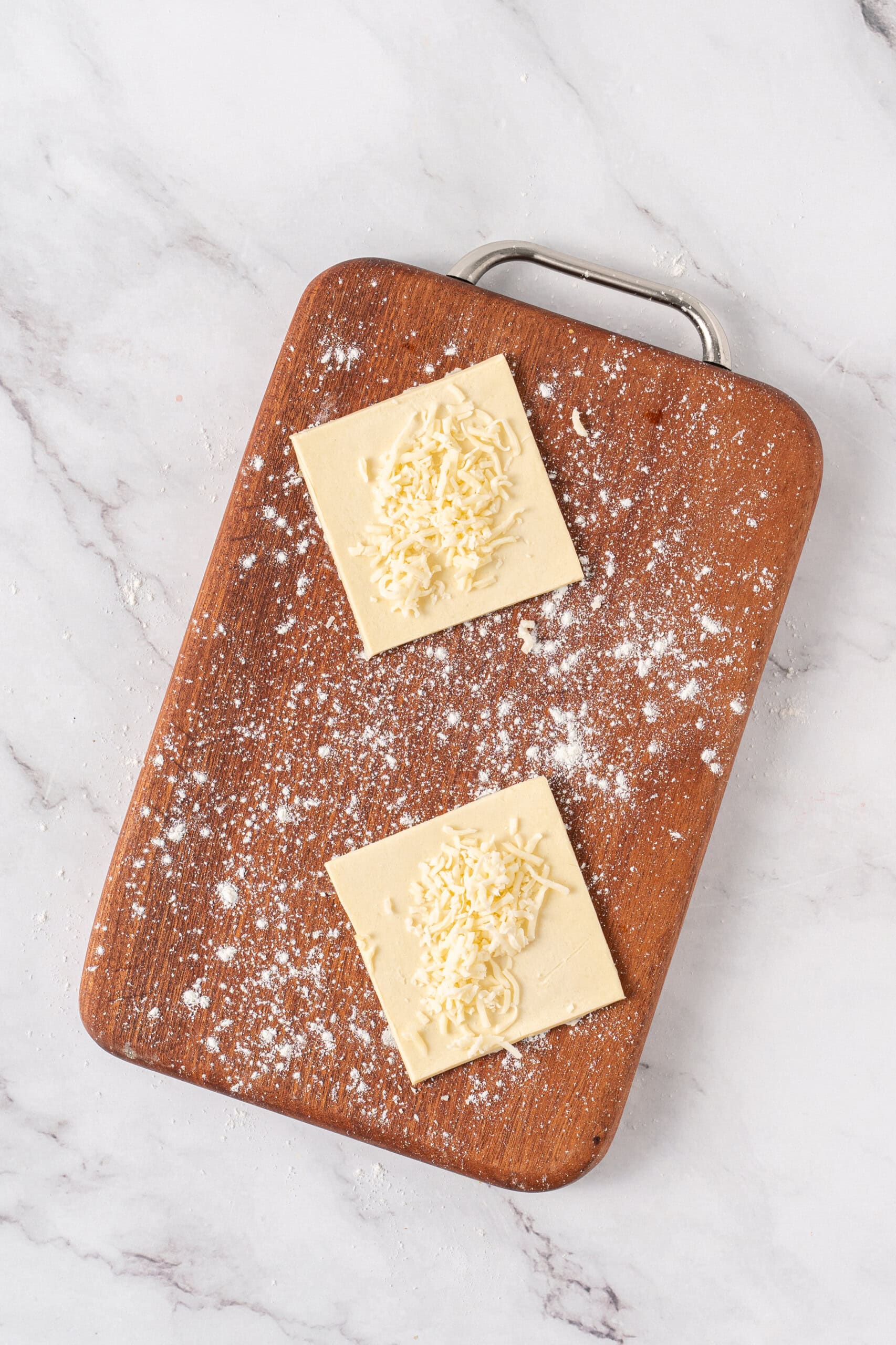 Puff pastry squares topped with shredded cheese on a lightly floured cutting board.