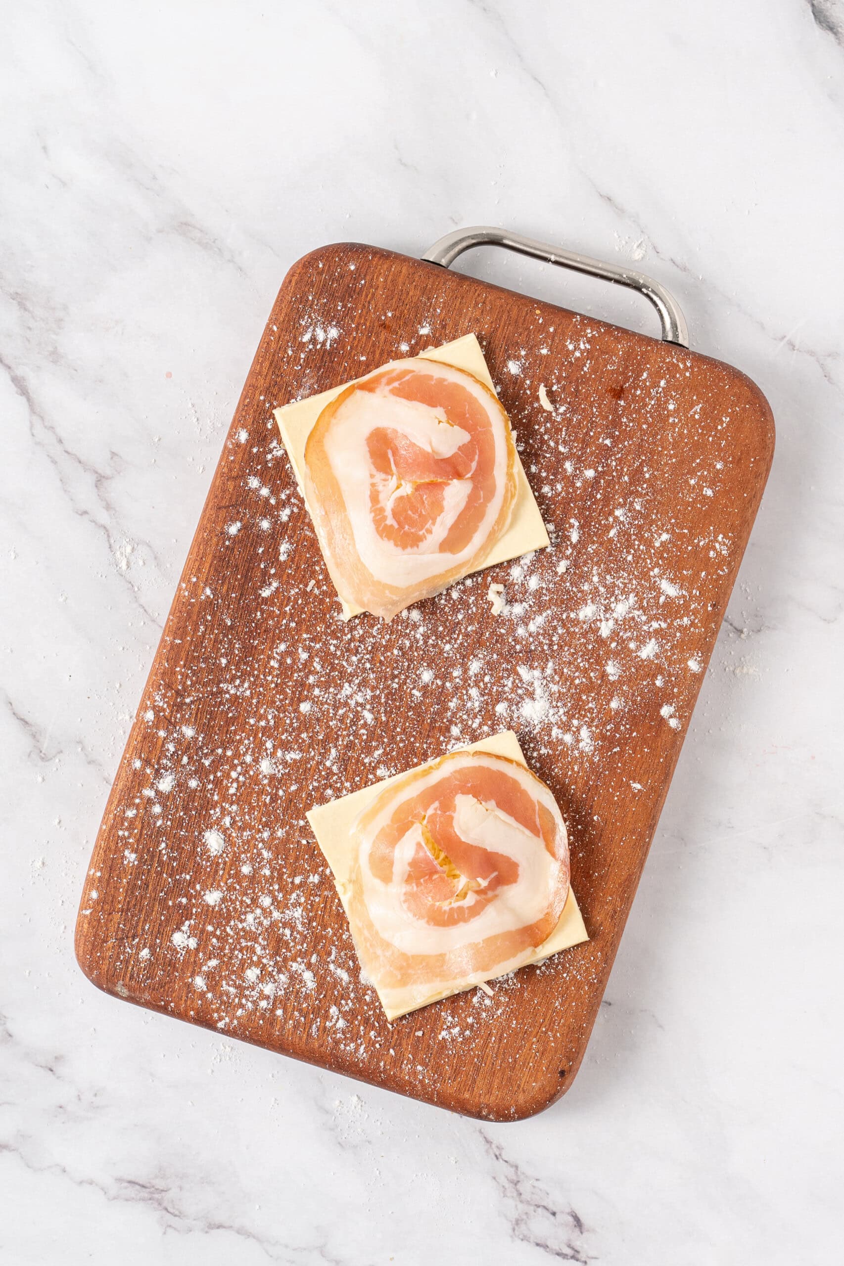 Puff pastry squares topped with pancetta on a lightly floured cutting board.